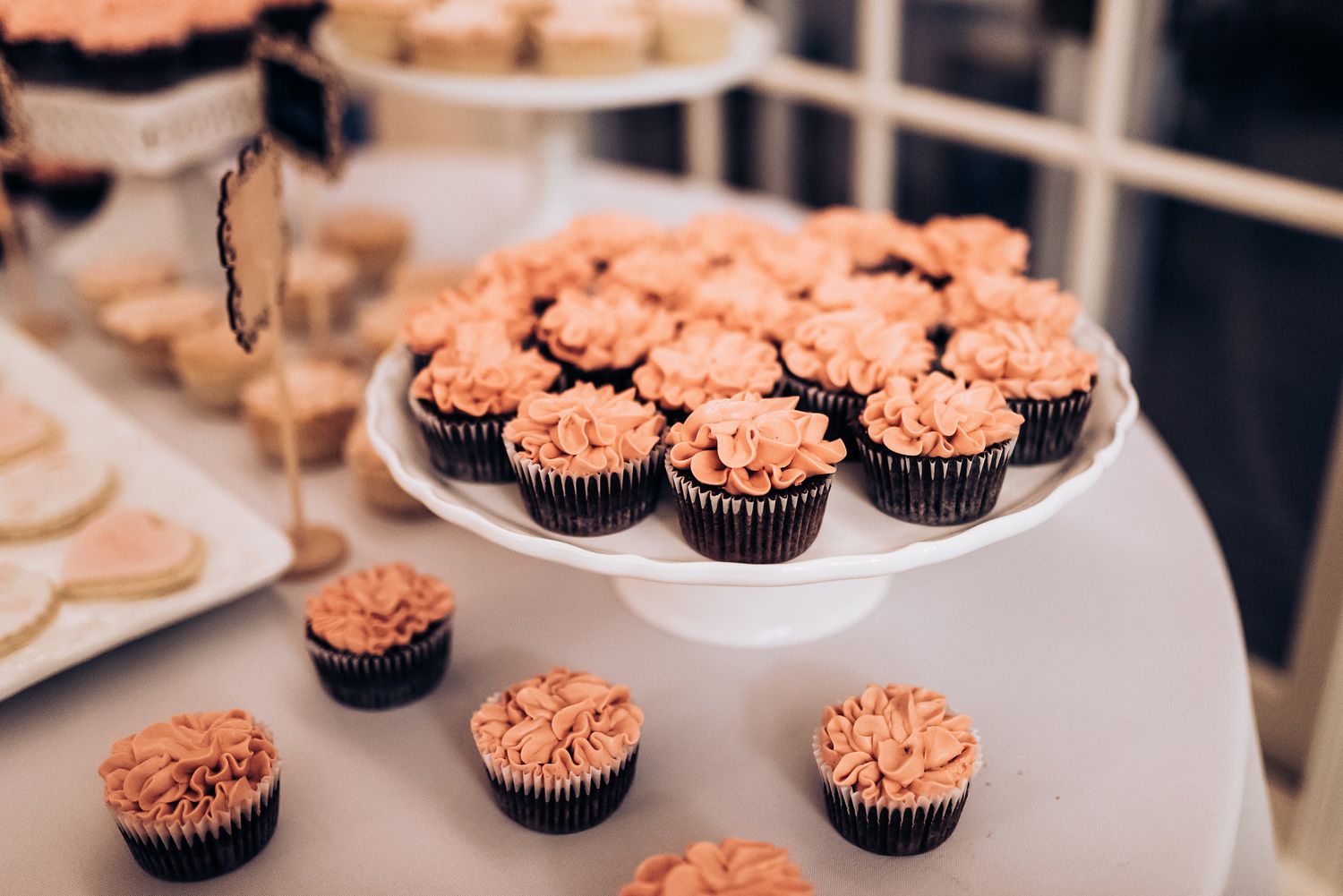 Pink frosted chocolate cupcakes displayed on a white cake stand at a wedding reception.