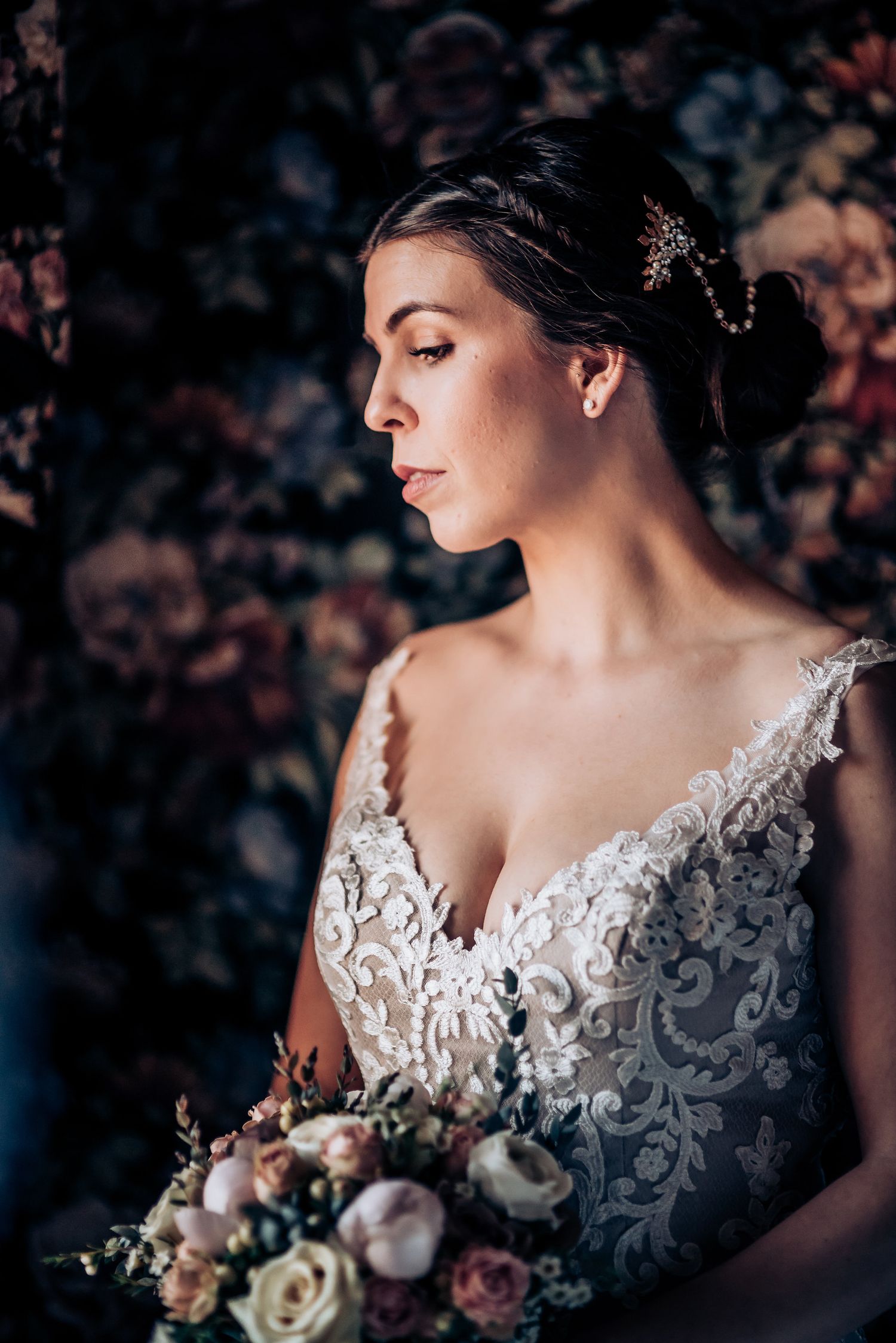 Dramatic side profile of a bride in lace against moody floral backdrop.
