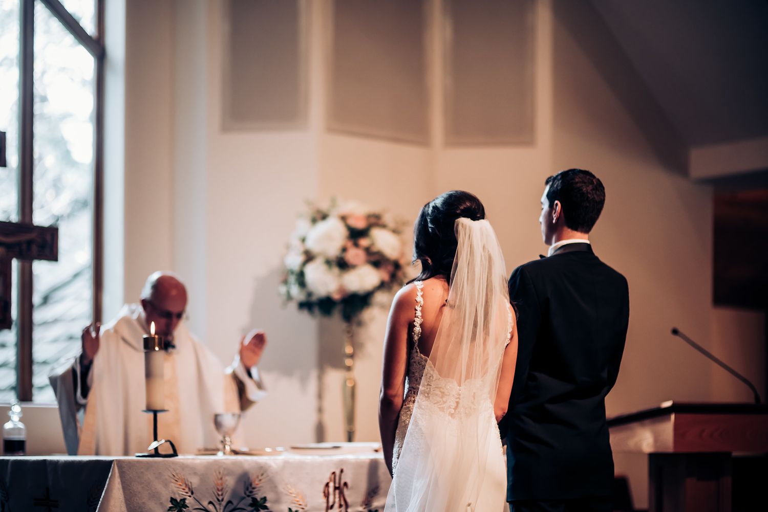 Wedding ceremony at church altar with floral arrangements and stained glass windows.