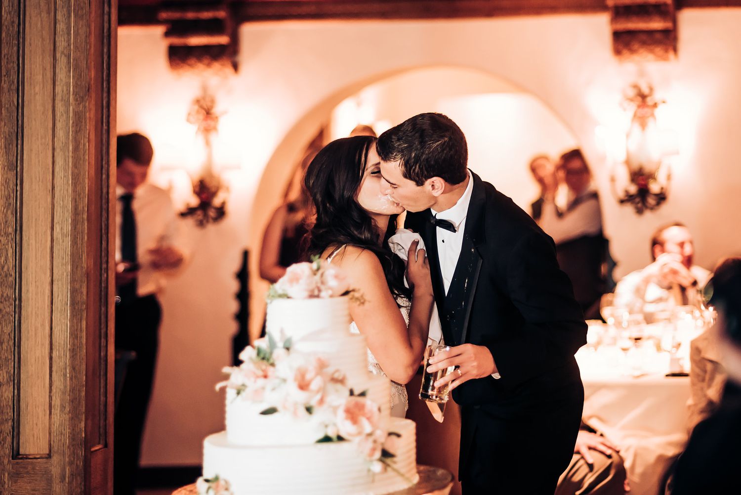 Romantic moment shared near an elegant tiered wedding cake at the reception.