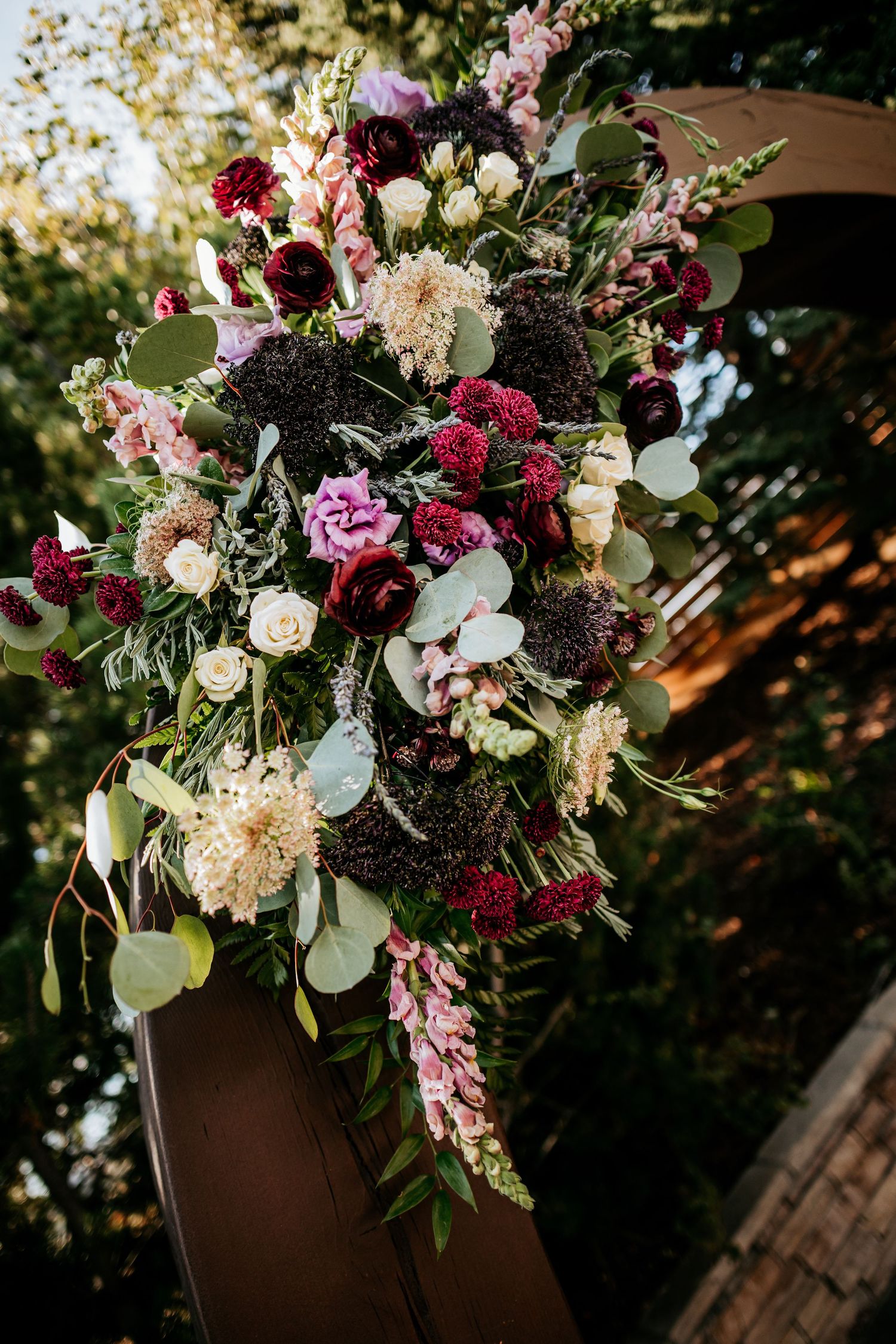Lush floral wedding arch arrangement with deep red, pink, and white blooms.