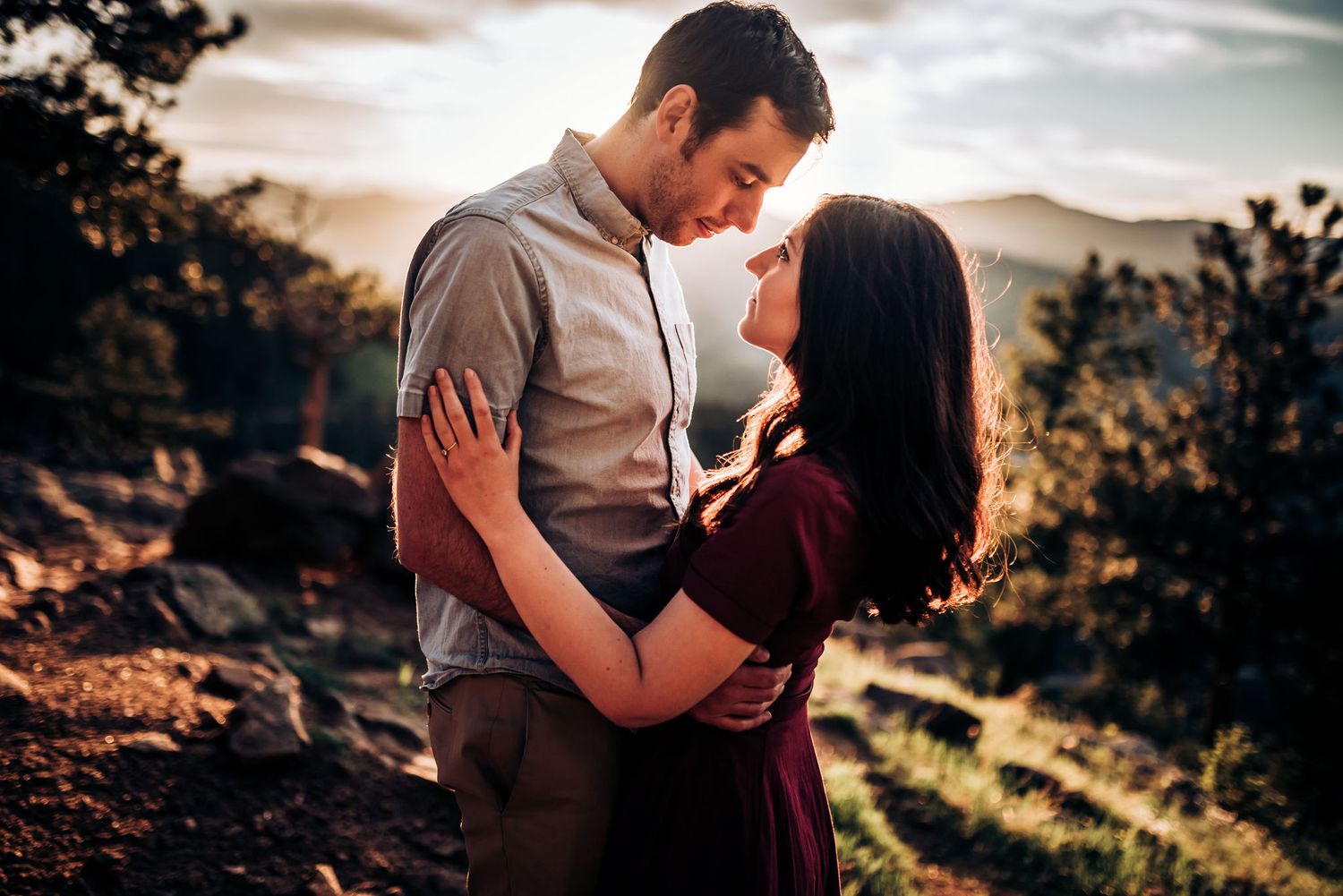 Couple in casual attire embracing on scenic mountain trail during sunset.