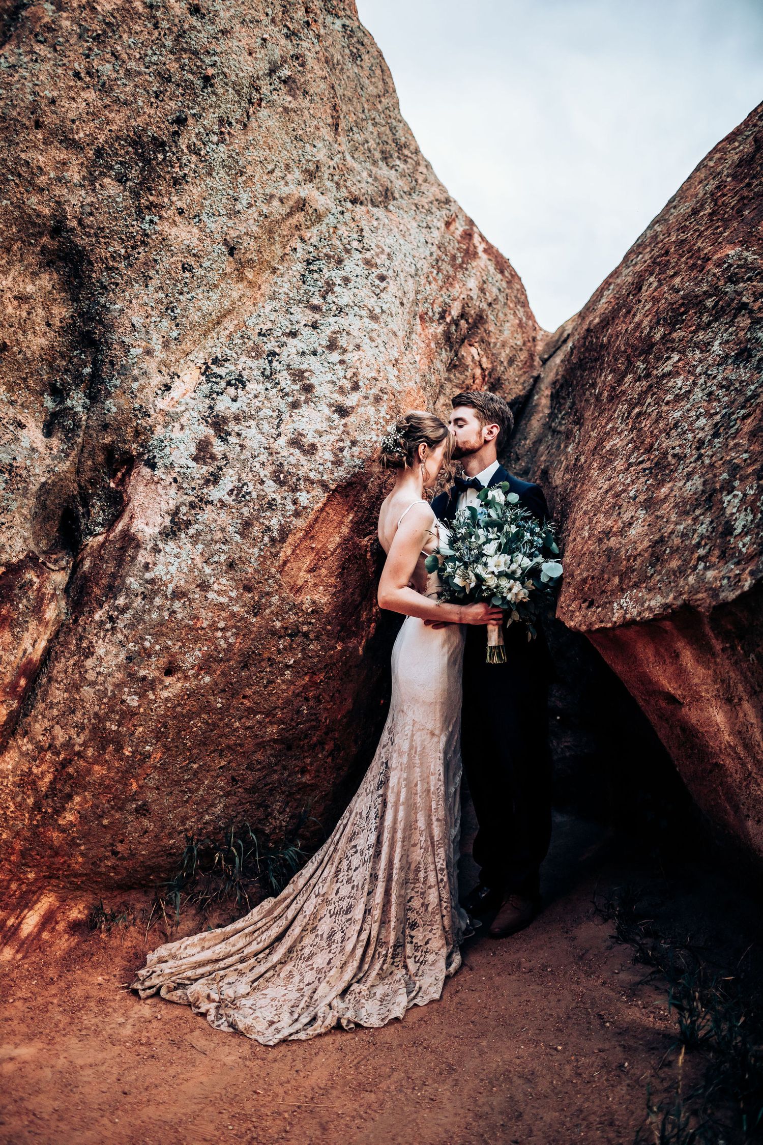 Elegant wedding portrait between towering red rock formations with flowing lace gown.
