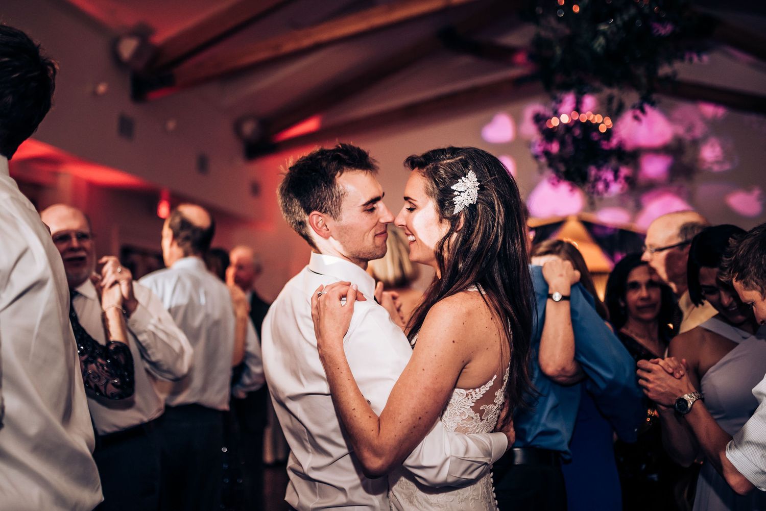 Romantic dance moment captured during wedding reception with pink ambient lighting and festive atmosphere.
