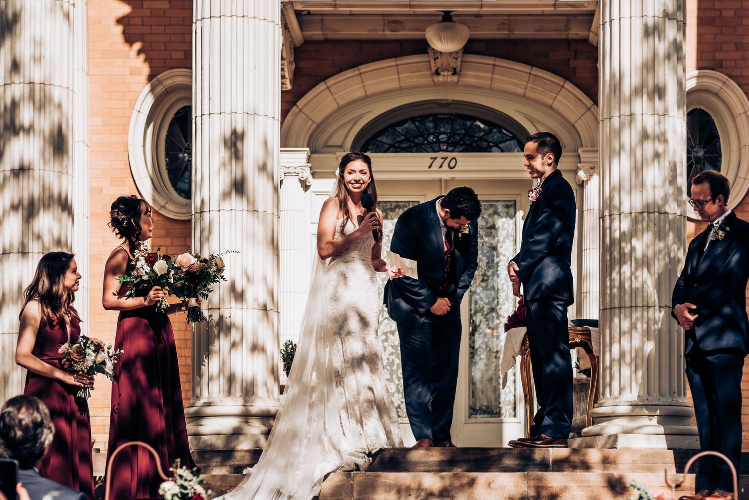 Outdoor wedding ceremony on historic building steps with white columns and brick facade.