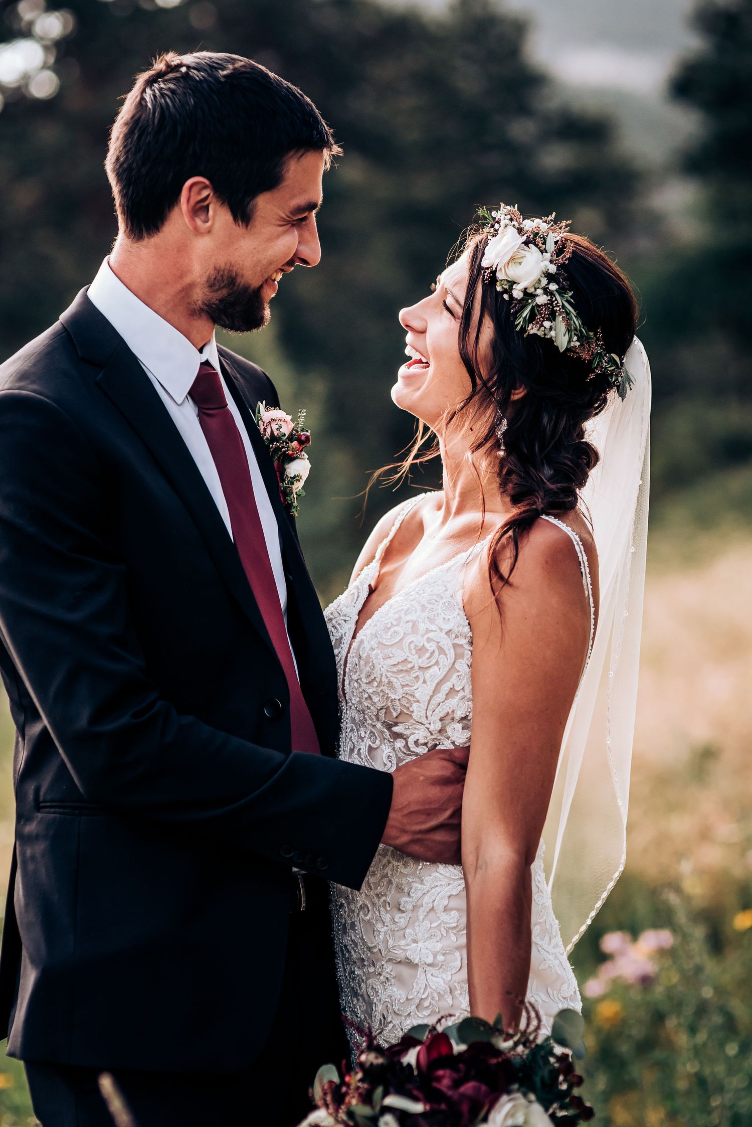 Joyful wedding portrait of couple laughing together in outdoor setting with floral crown and lace dress.