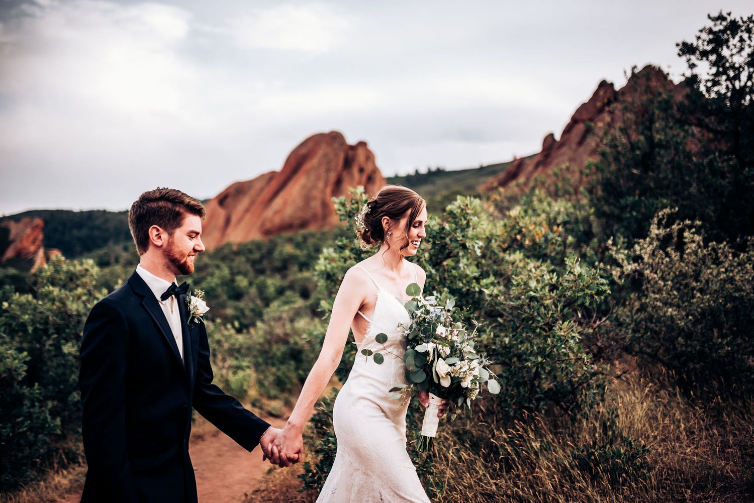 Couple holds hands while walking on trail with red rock formations at Garden of the Gods.
