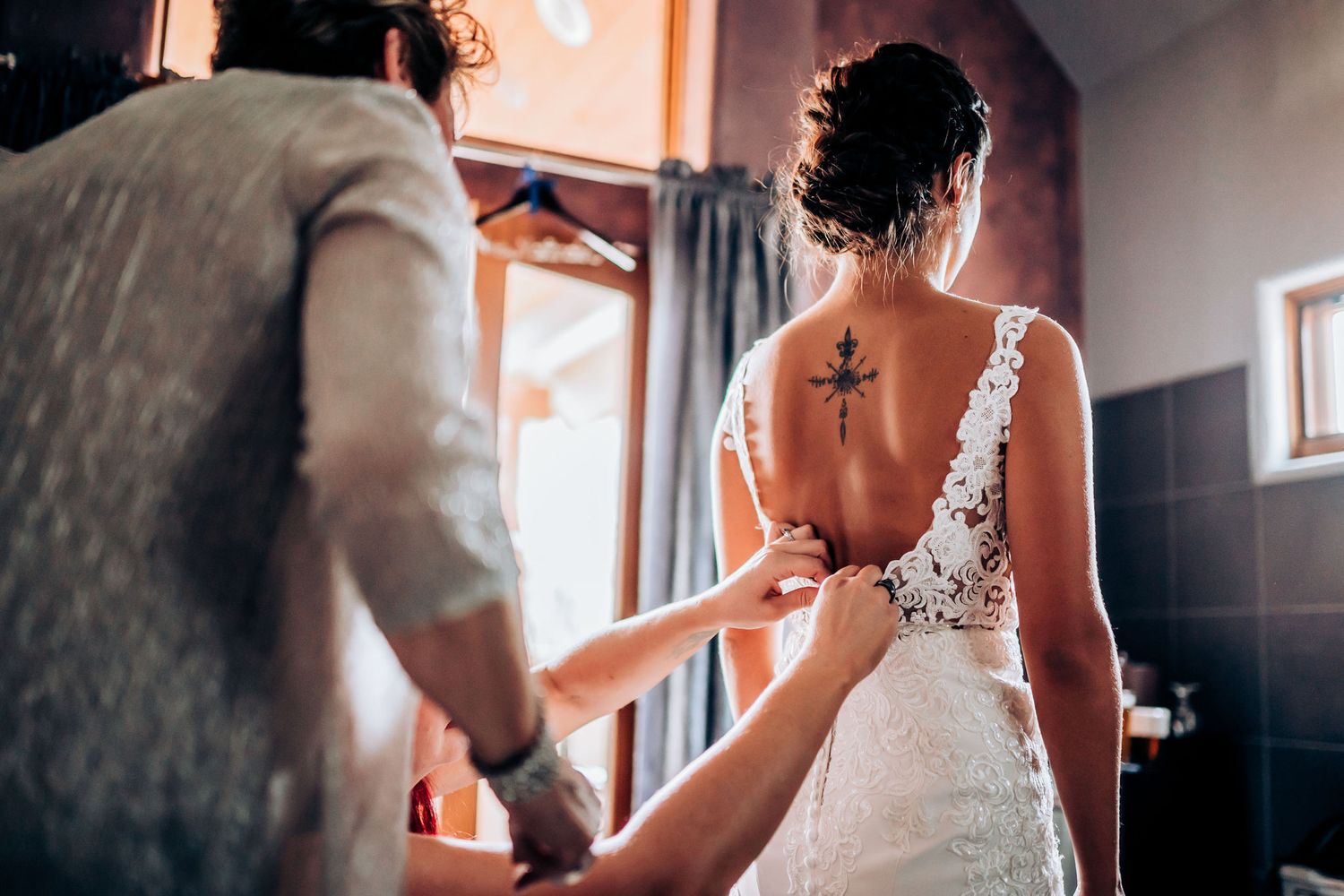 Back view of white lace wedding dress being fastened during preparation.