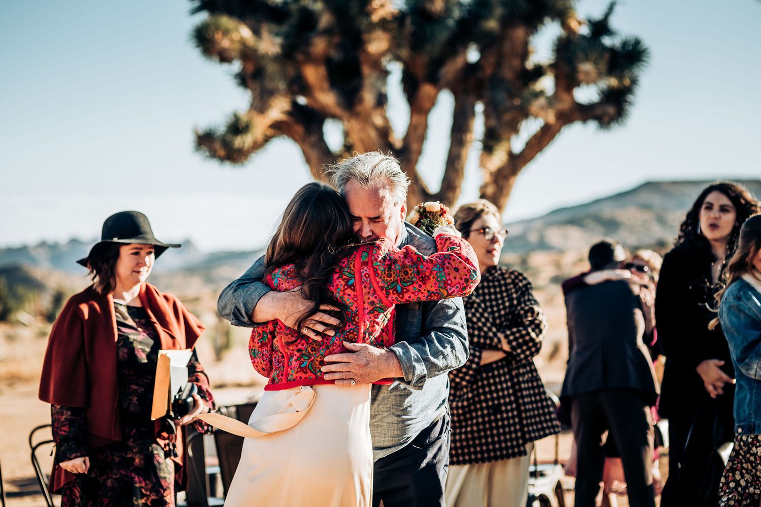 Wedding celebration with embraces and hugs under a Joshua Tree in the desert.