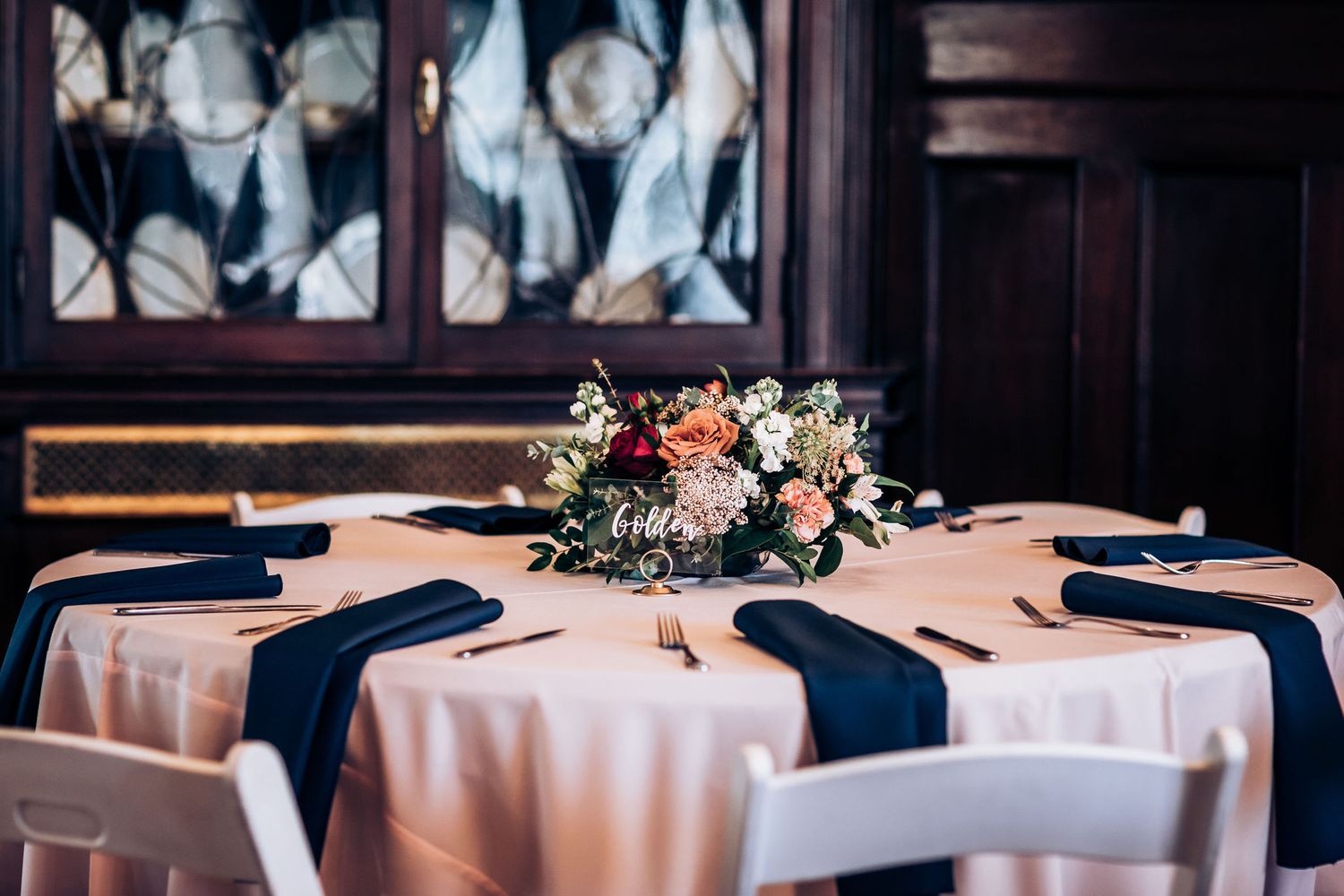 Elegant table setting with navy blue runners and floral centerpiece at formal event.