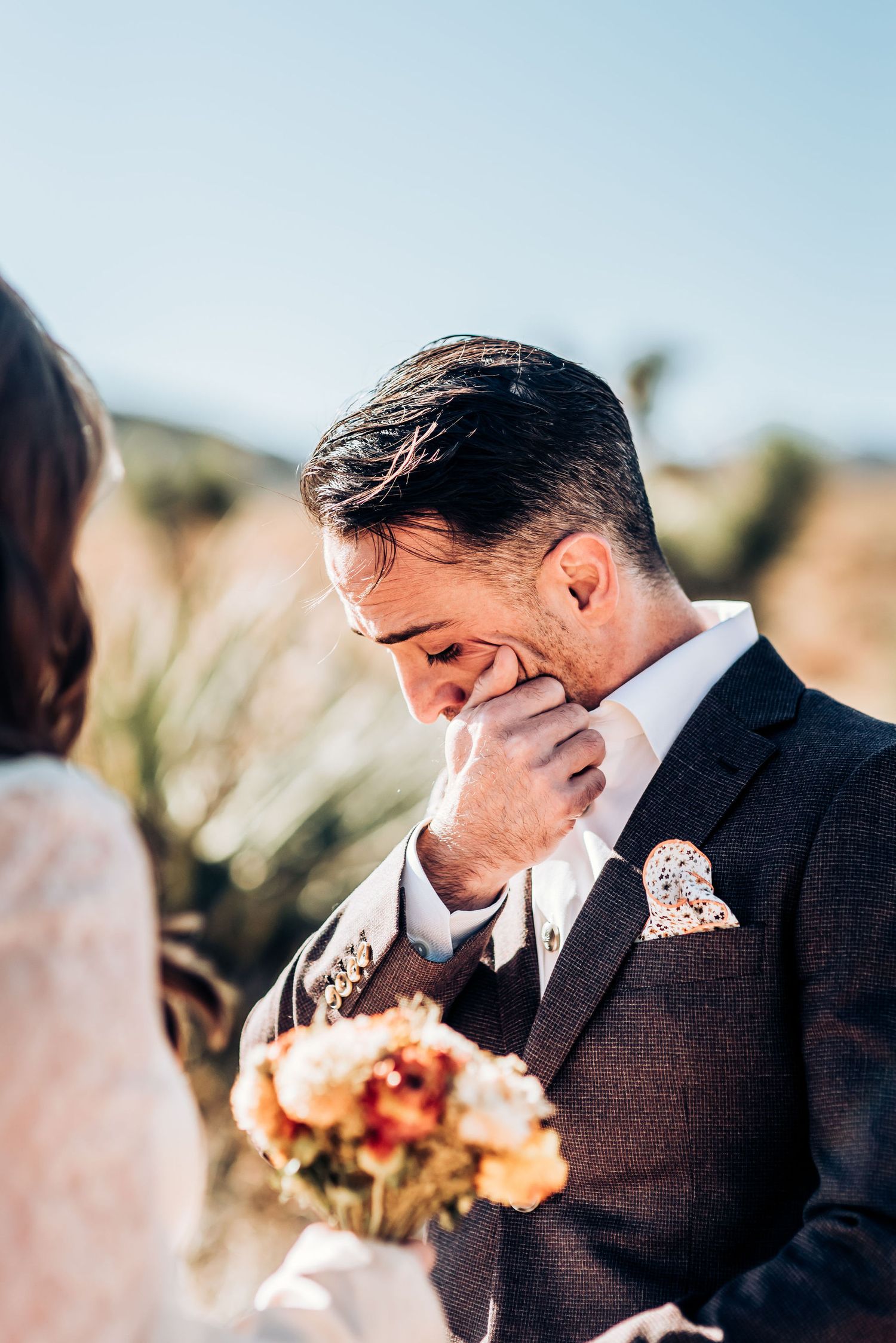 Emotional wedding moment captured during desert ceremony with bright sunlight.