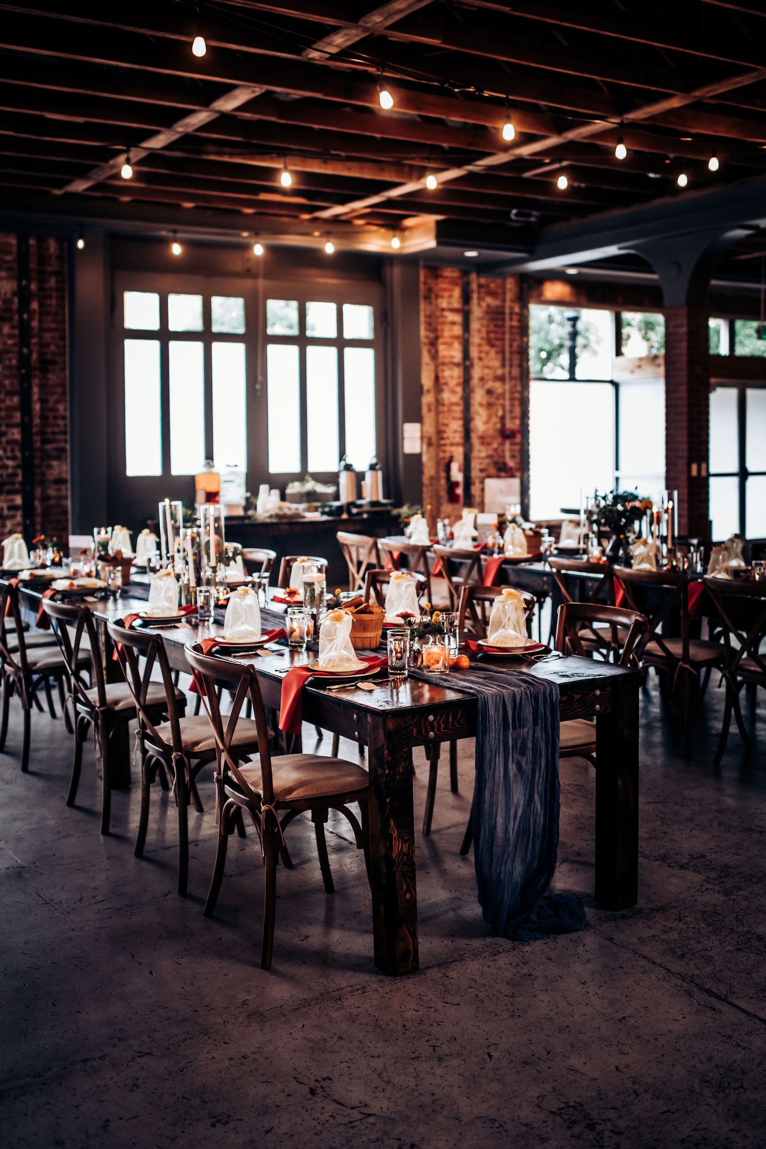 Industrial wedding venue with exposed brick walls and cross-back chairs set for reception dinner.