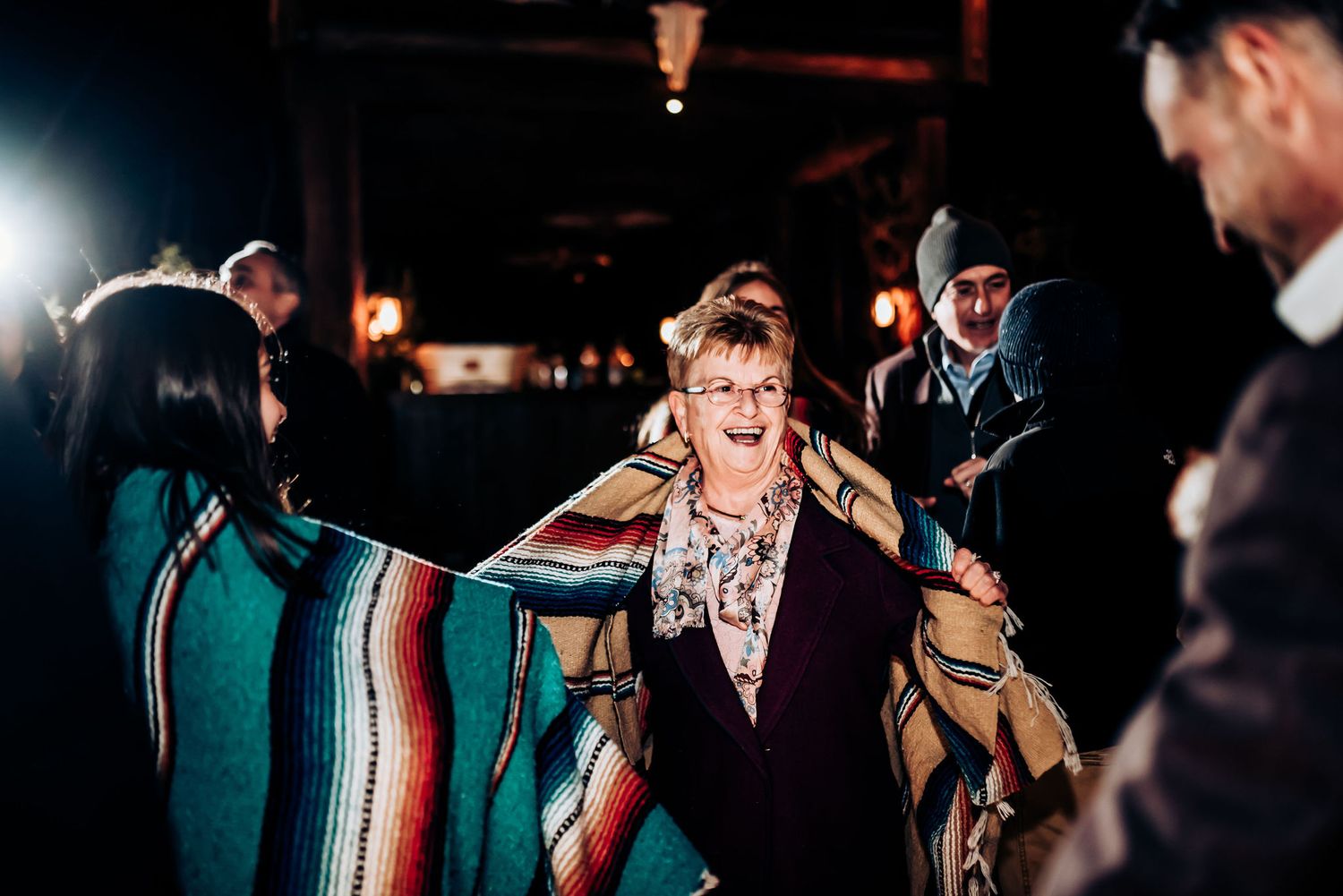Someone dances while wearing a colorful striped blanket at a nighttime event.