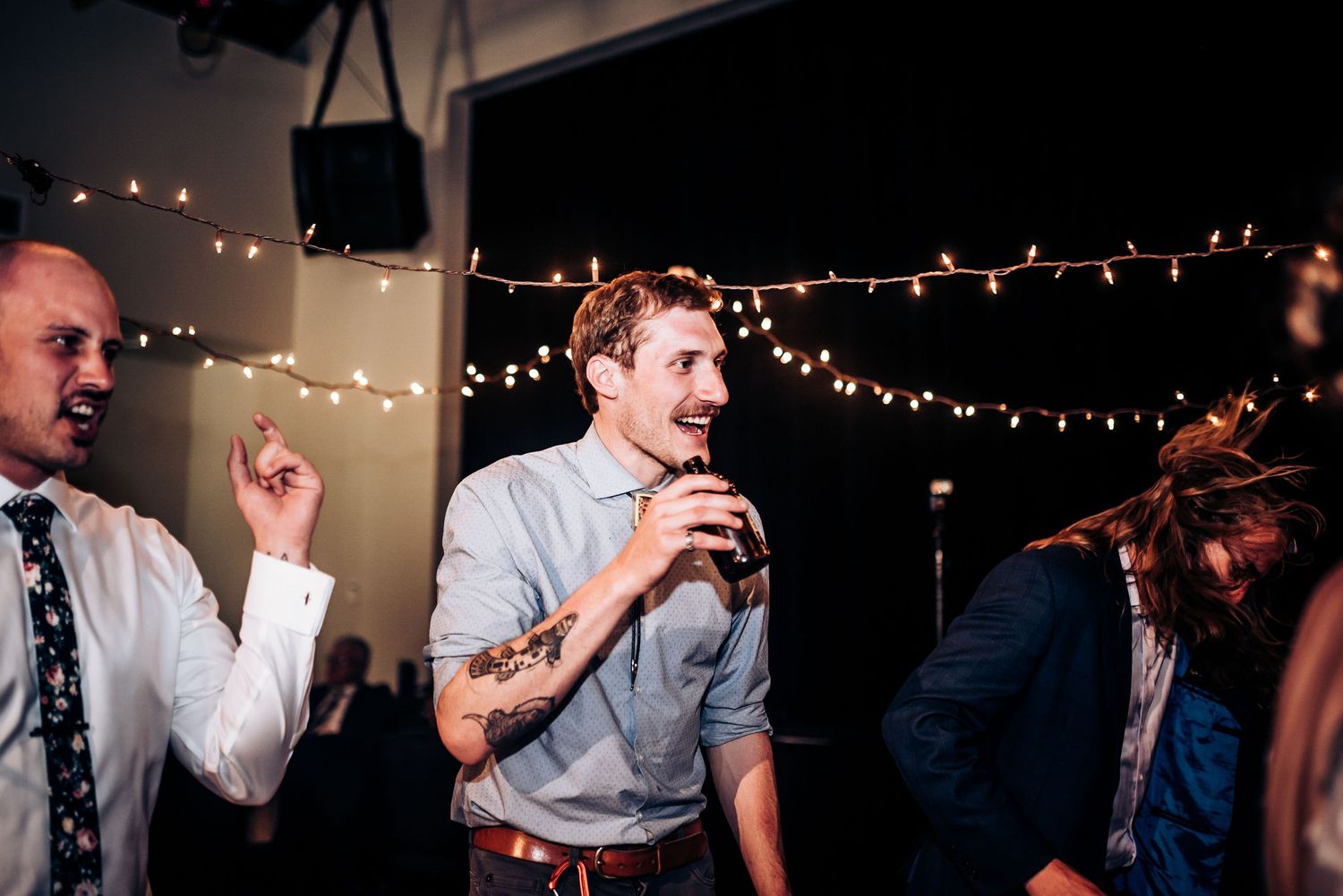 Wedding party guests dancing with dramatic string lights overhead at an indoor reception celebration.
