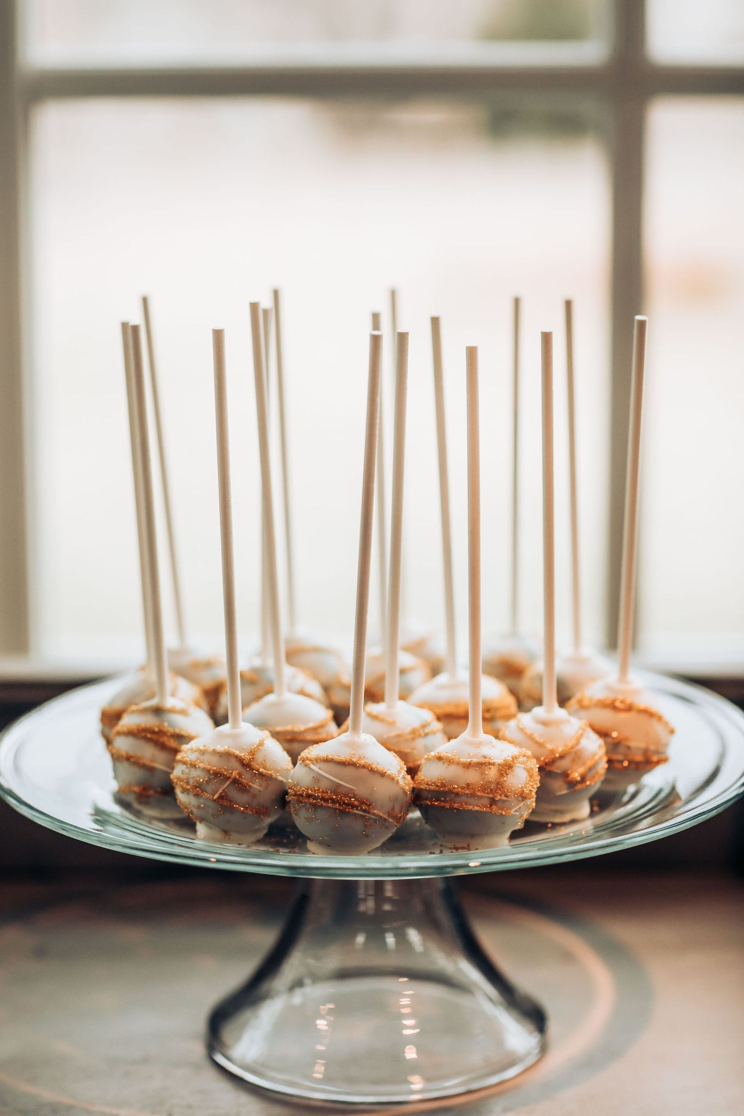 Mini desserts with long decorative sticks arranged on a glass cake stand.