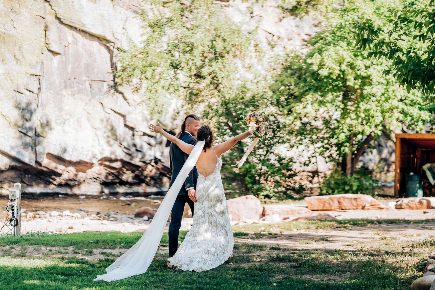 Romantic outdoor wedding portrait with couple dancing against stone cliff background.
