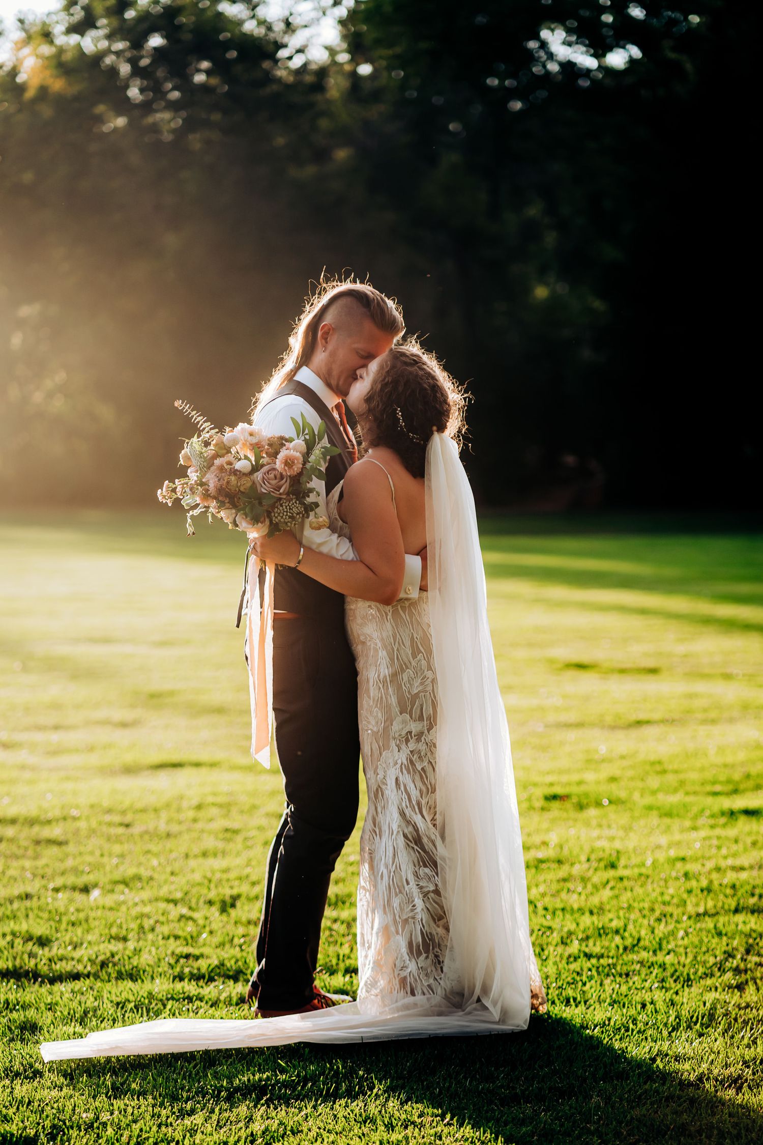 Sunset wedding portrait with couple holding bouquet on grassy lawn.