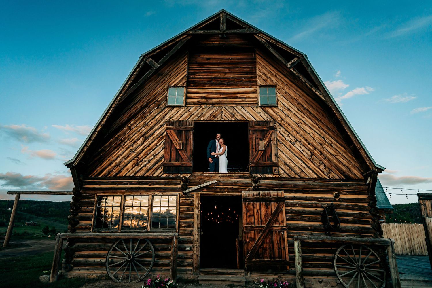 A rustic wooden barn with a gambrel roof stands against a vibrant blue sky in a rural setting.