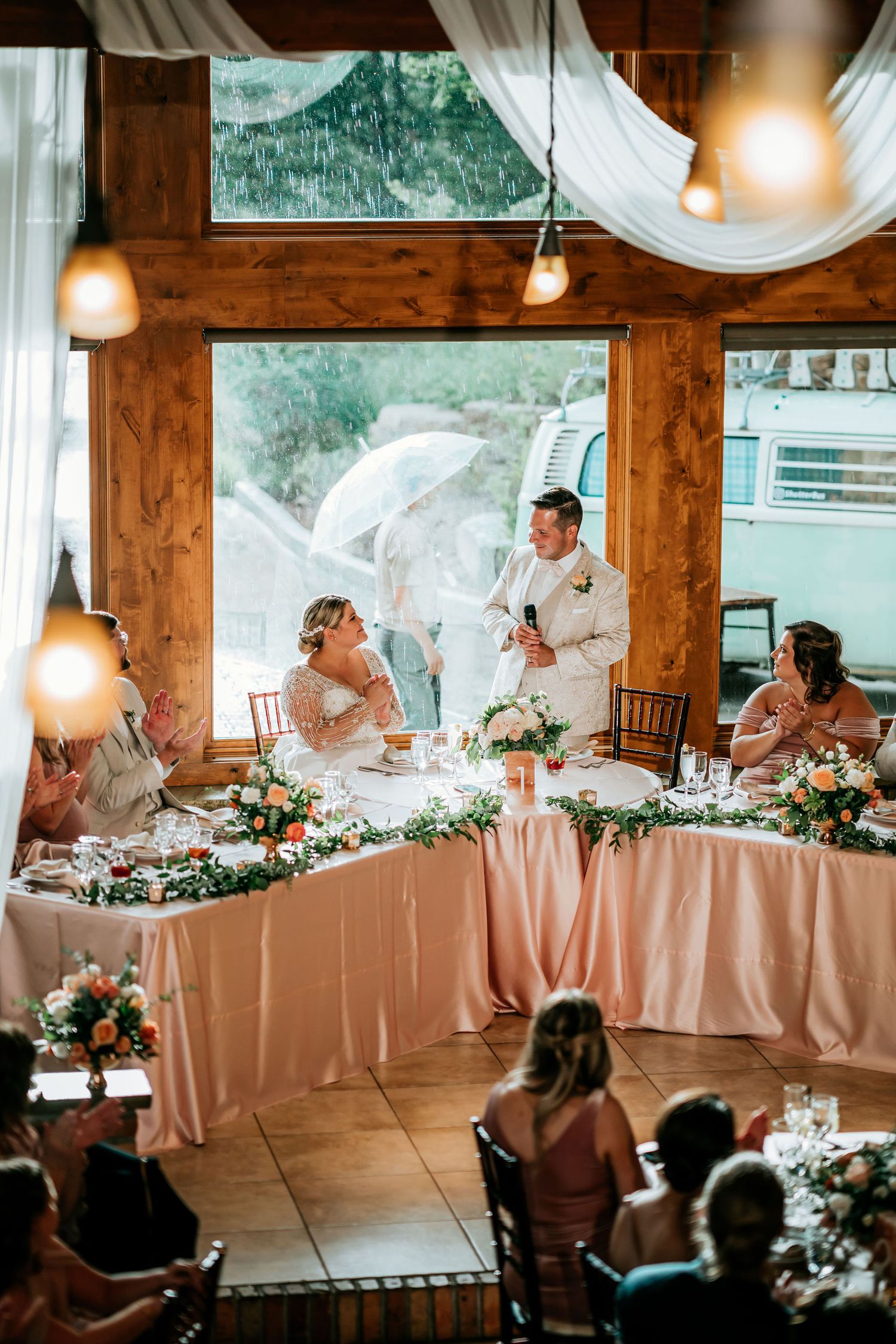 Wedding reception in rustic wooden venue with hanging lights and mountain views through large windows.