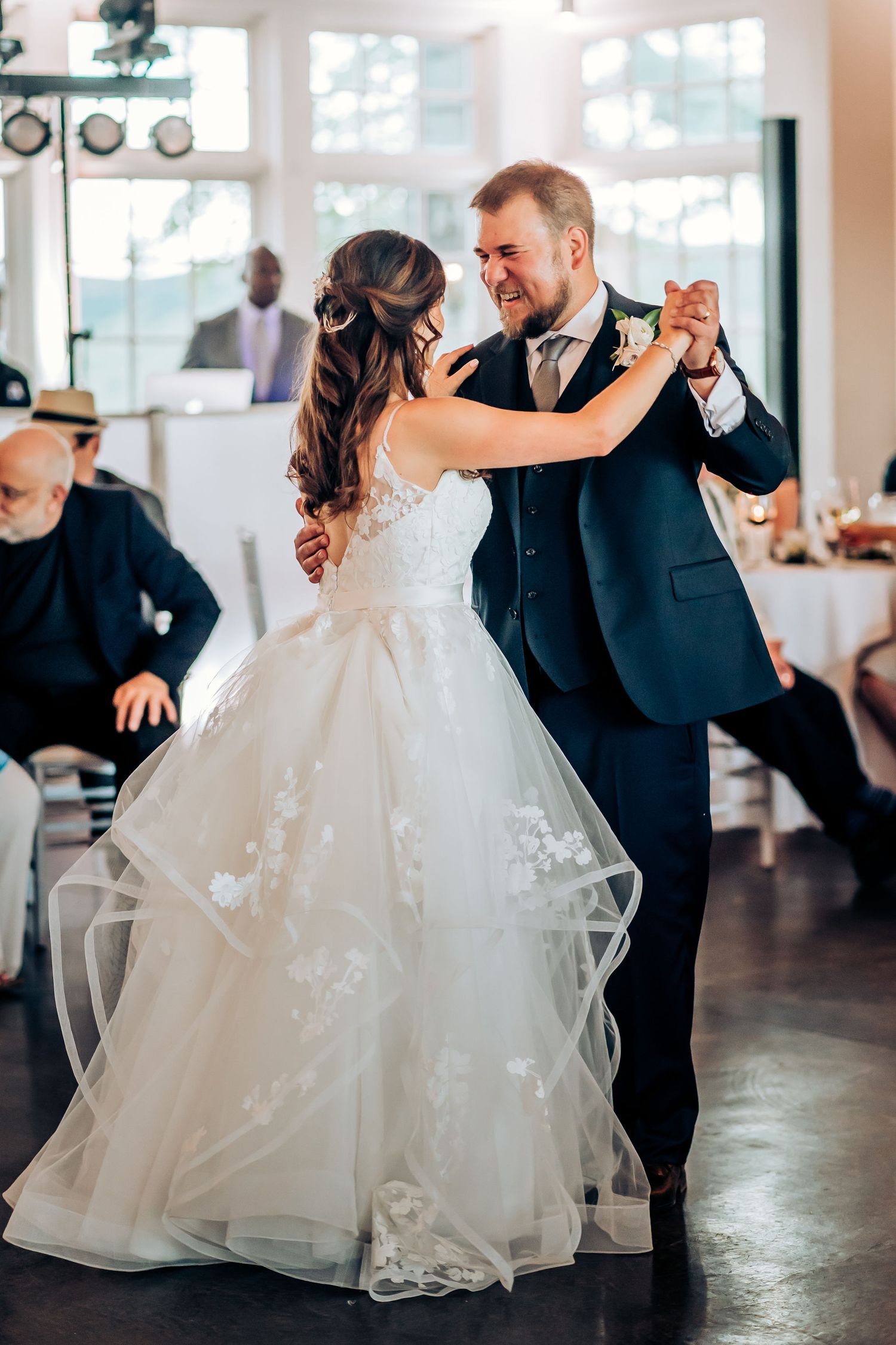Wedding couple shares intimate dance moment on dark floor with natural window light.