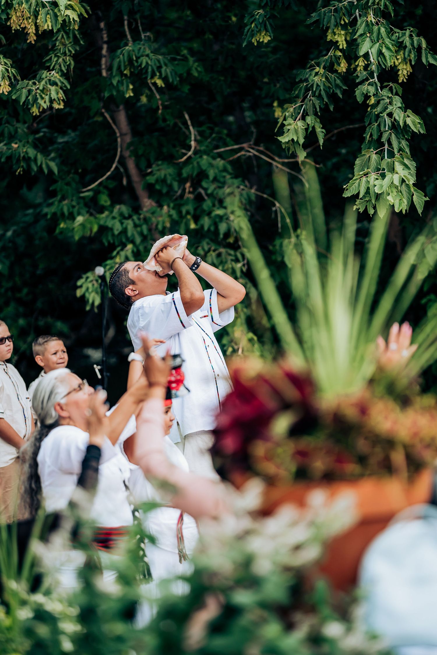 Person with microphone singing or speaking during outdoor wedding celebration with raised hands in crowd.