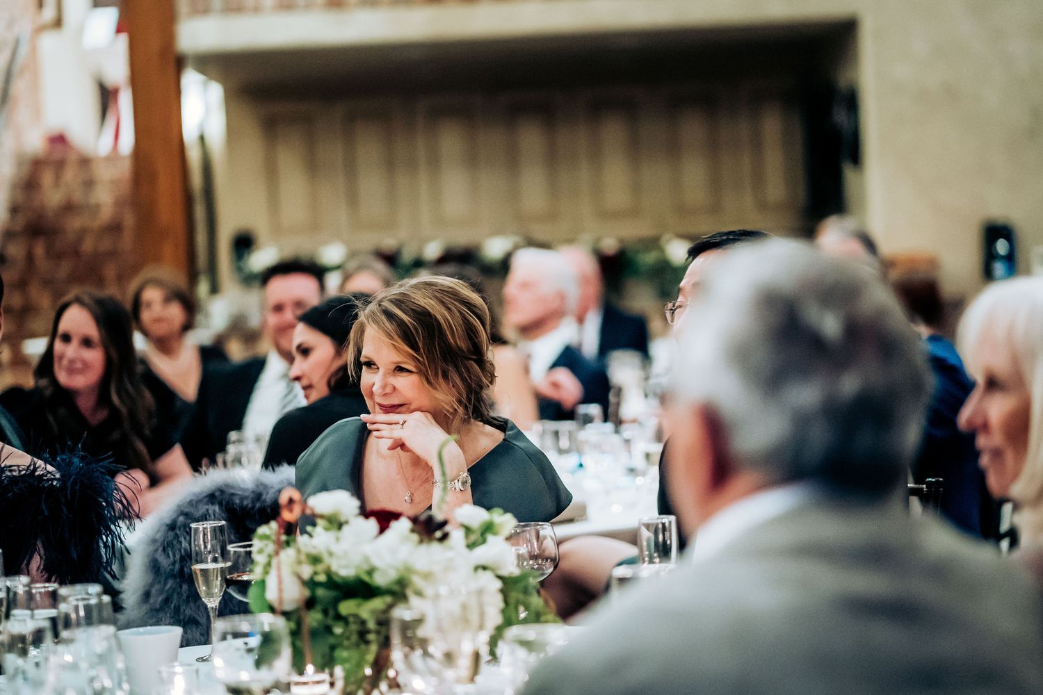 Wedding reception guests enjoying dinner at decorated tables with floral centerpieces.