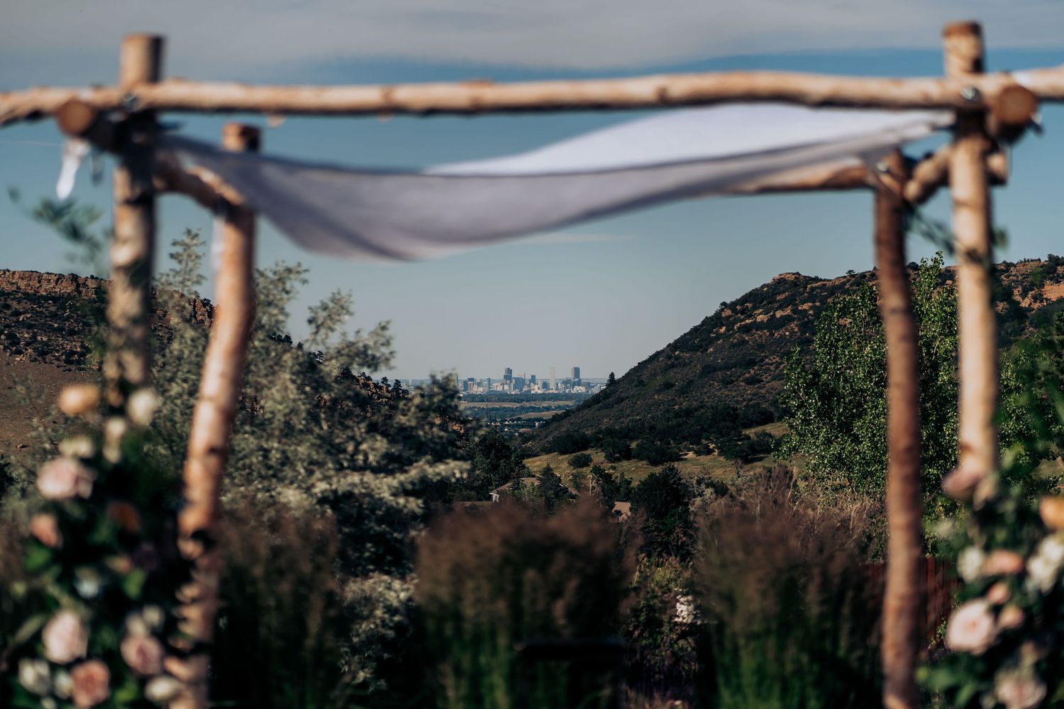 Rustic wooden arch with flowing fabric overlooking mountain valley landscape.