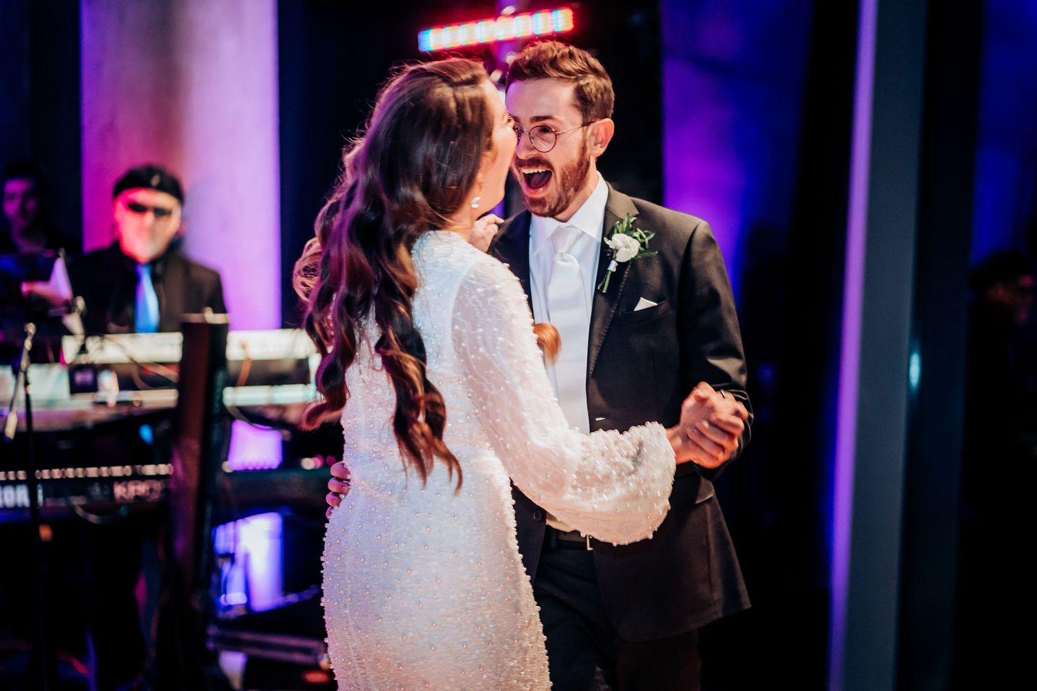 A couple shares a joyful moment while dancing at their wedding reception with band in background.