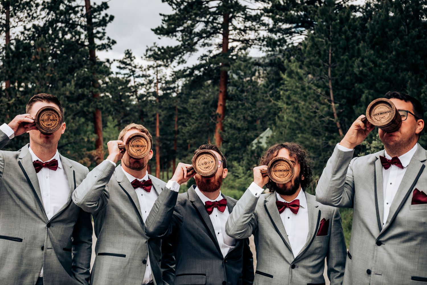 Groomsmen in matching gray suits and bowties playfully pose while looking through imaginary binoculars.