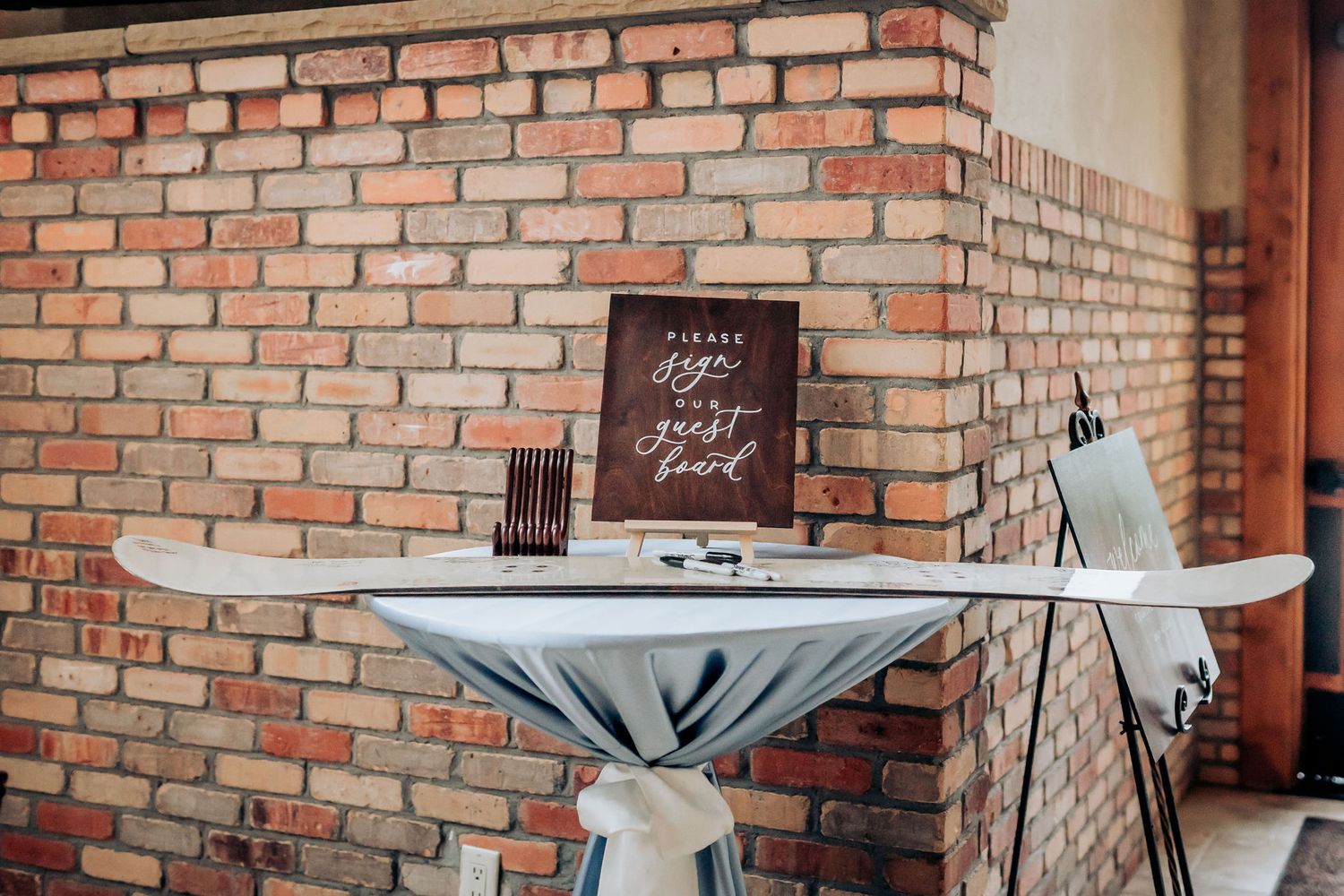 A guest book table setup against a brick wall with vintage decor.
