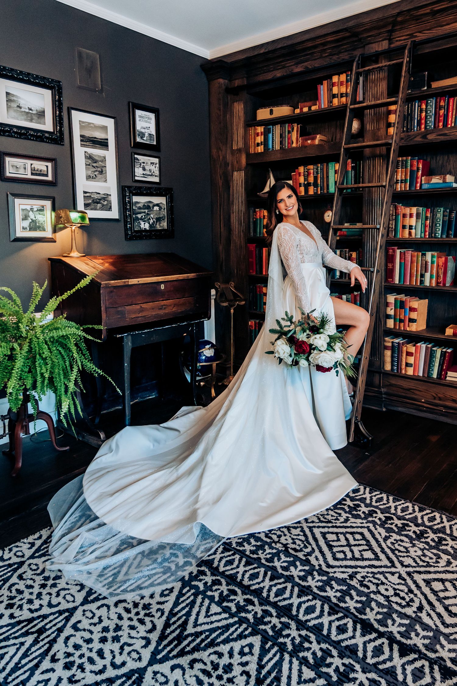 A bride poses with her wedding dress train arranged on a geometric patterned rug in a library setting.