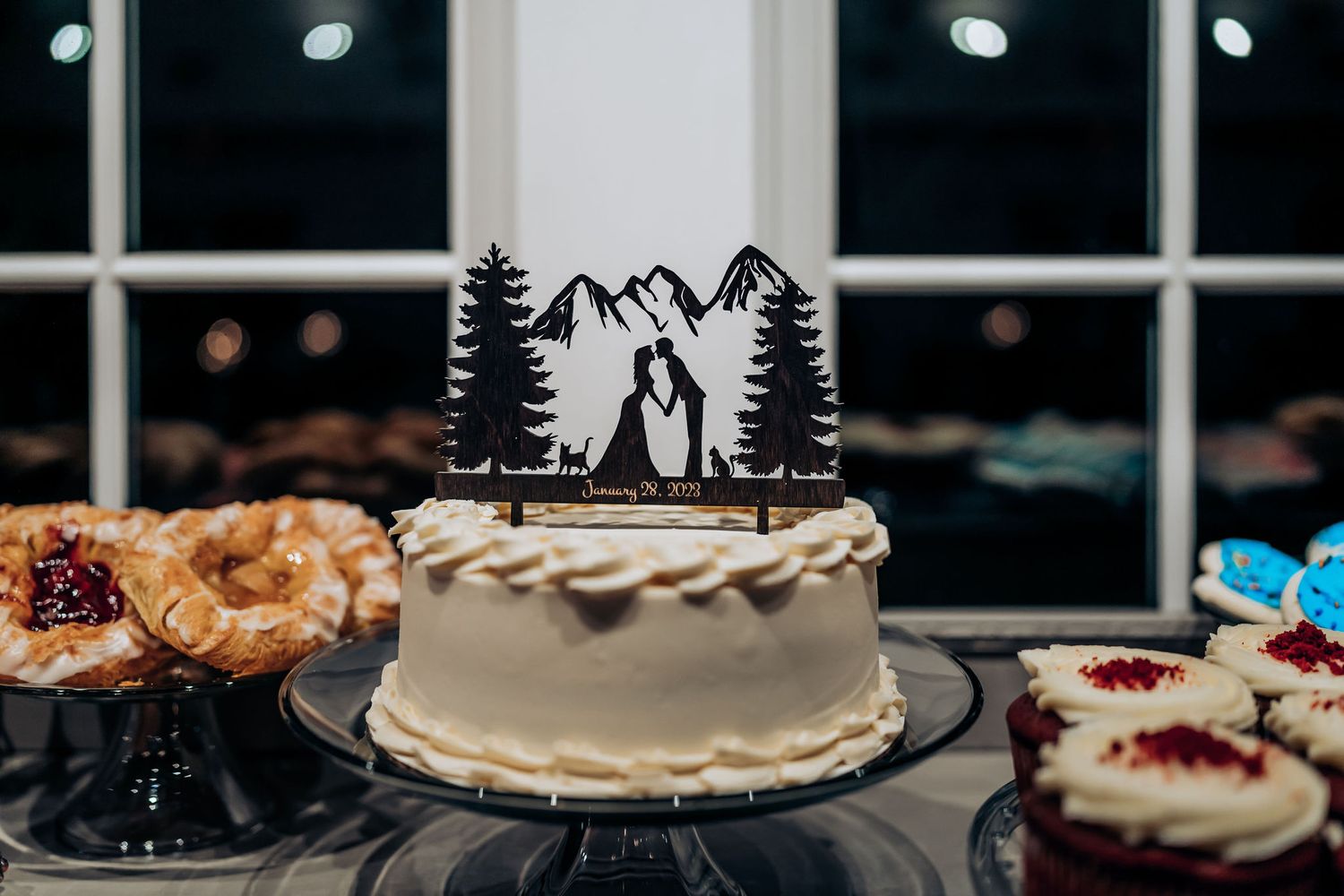 White wedding cake topped with mountain-themed silhouette cake topper.