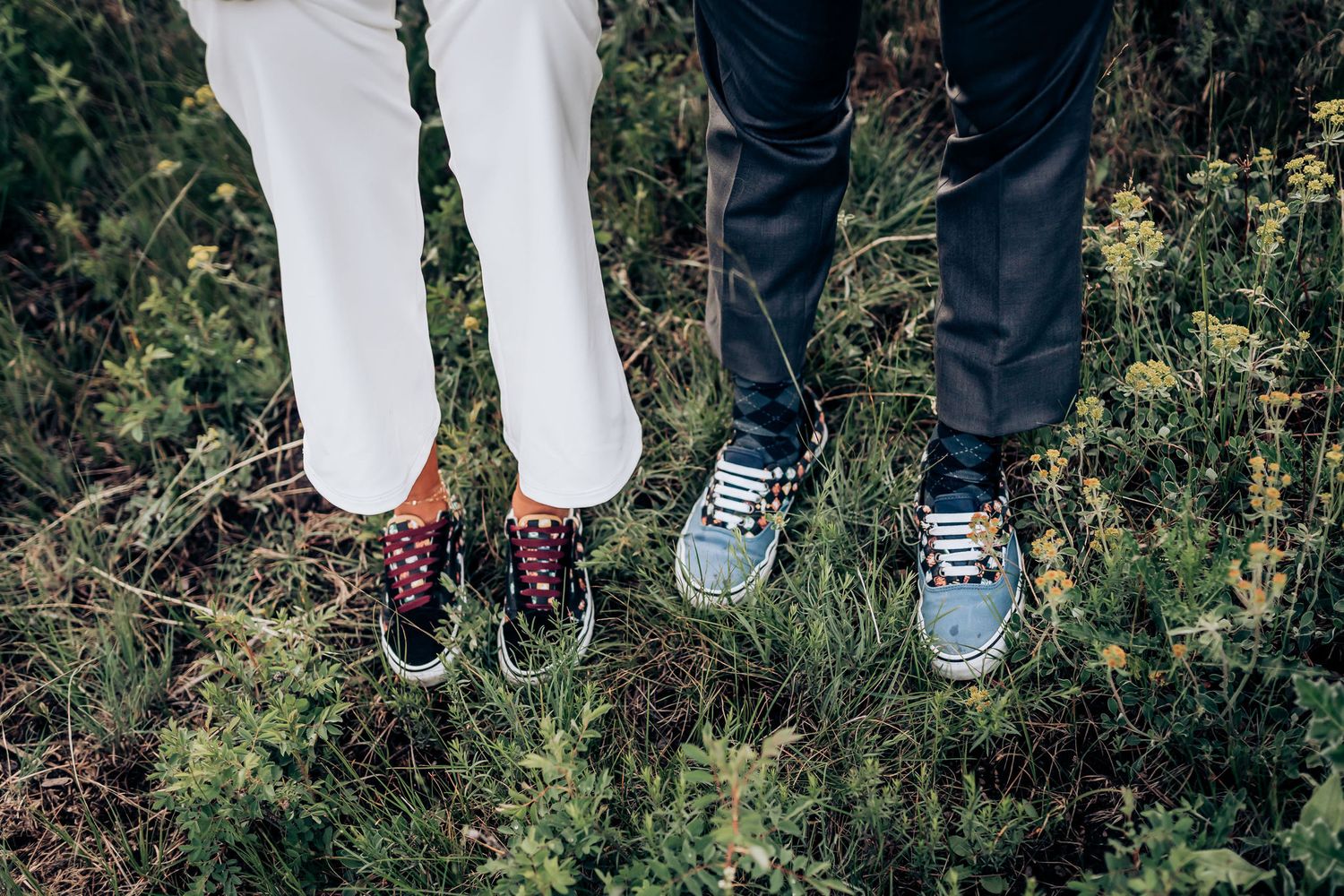 Close-up of sneakers and shoes of a couple standing in grass, showing playful footwear choices.