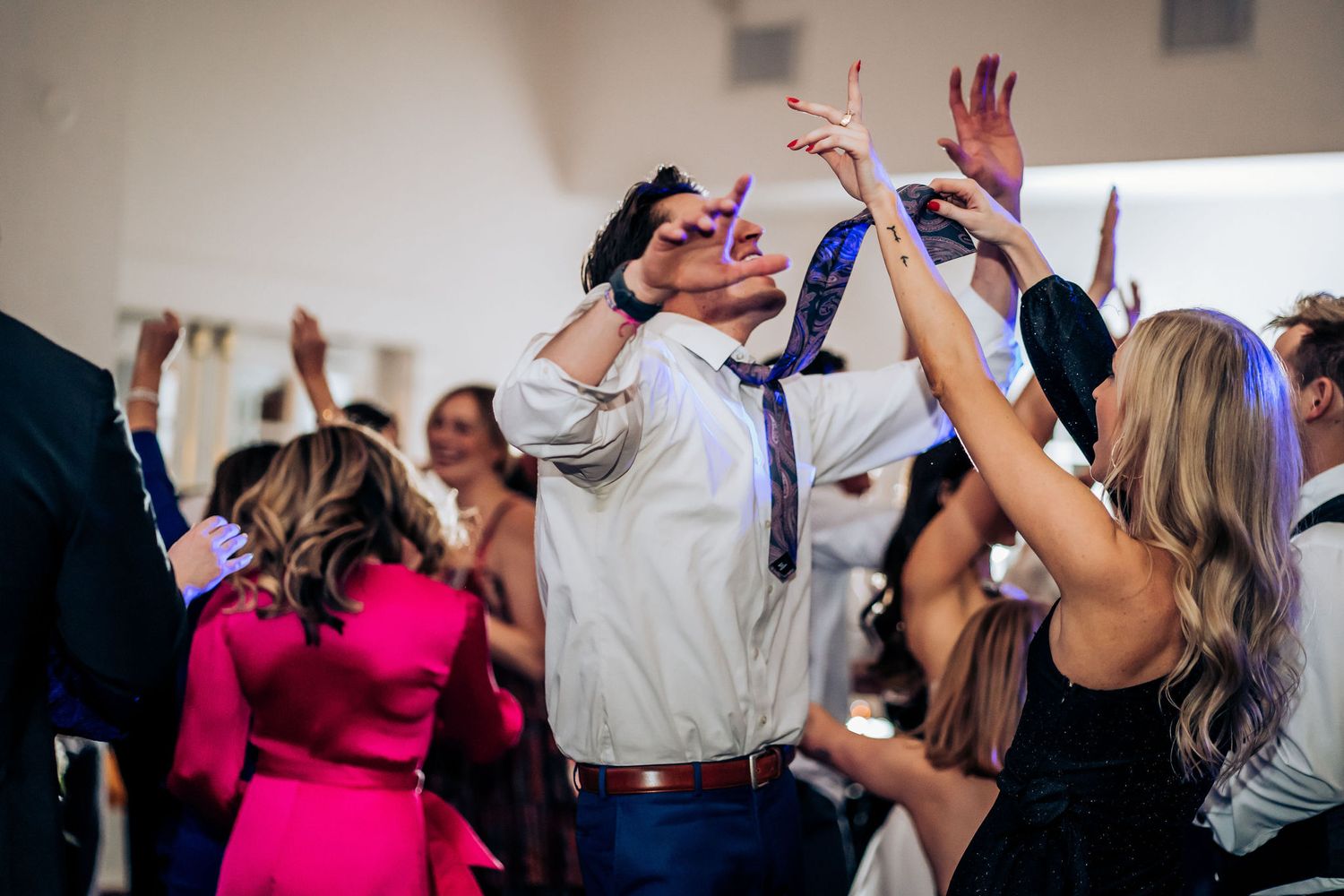 Energetic dancing and celebration during wedding reception with guests raising hands in the air.
