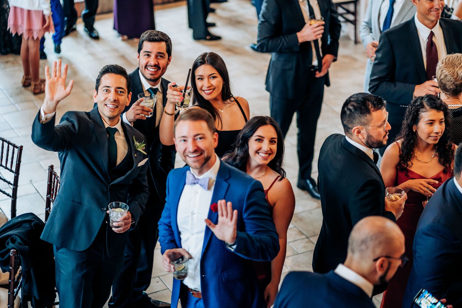 Wedding guests in formal attire celebrating and waving at the reception venue.