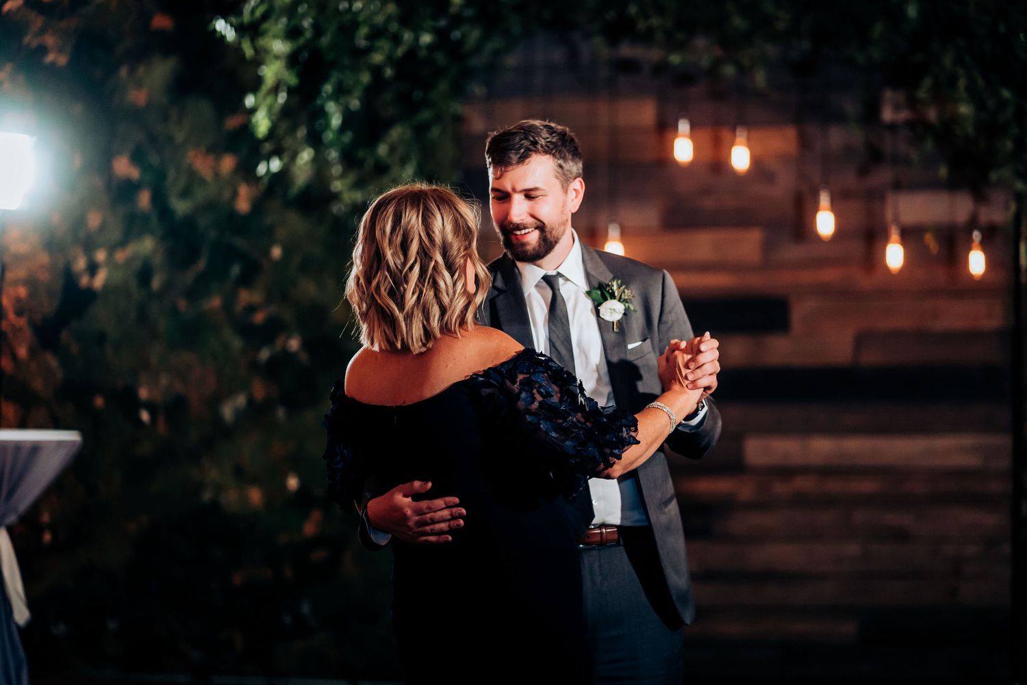 Couple sharing intimate dance moment under romantic evening lighting with rustic backdrop.