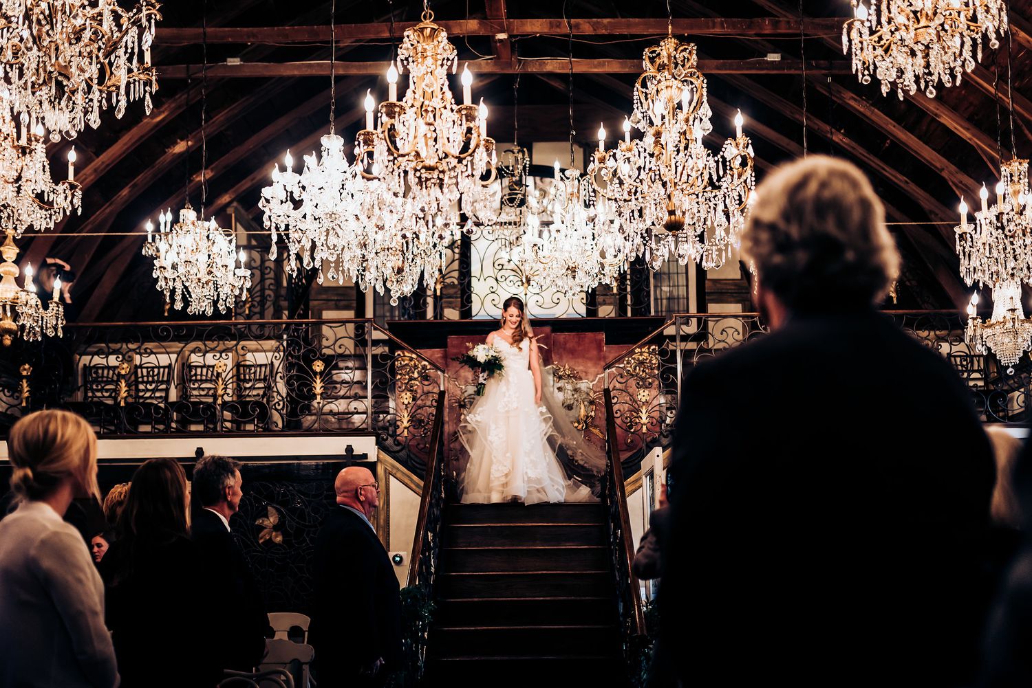 Wedding ceremony in progress under crystal chandeliers with guests watching from below.