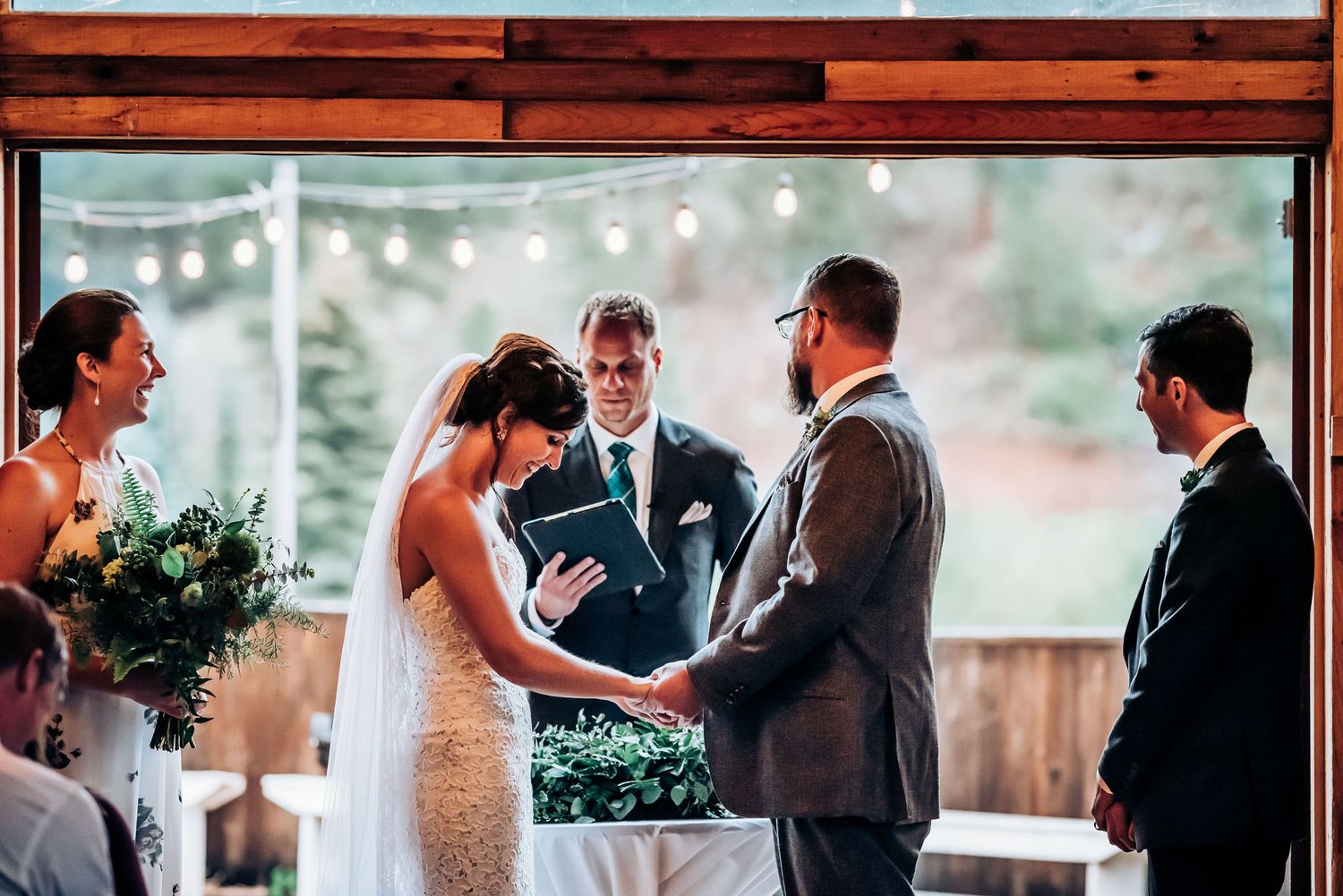Wedding ceremony under wooden beams with string lights and natural lighting.