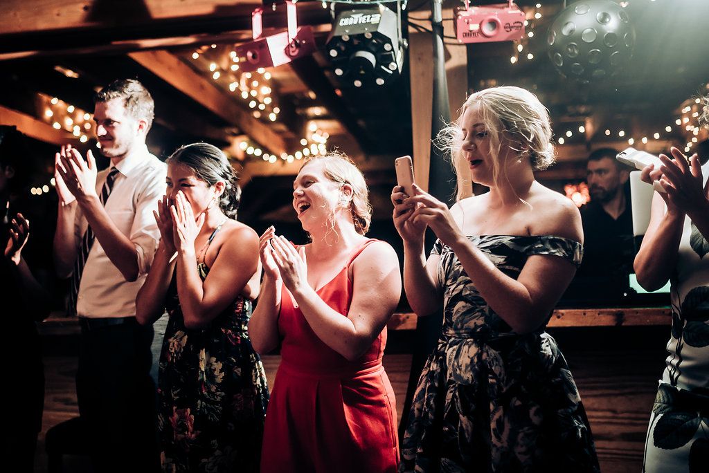 Party attendees clap and celebrate under decorative string lights at an indoor venue.