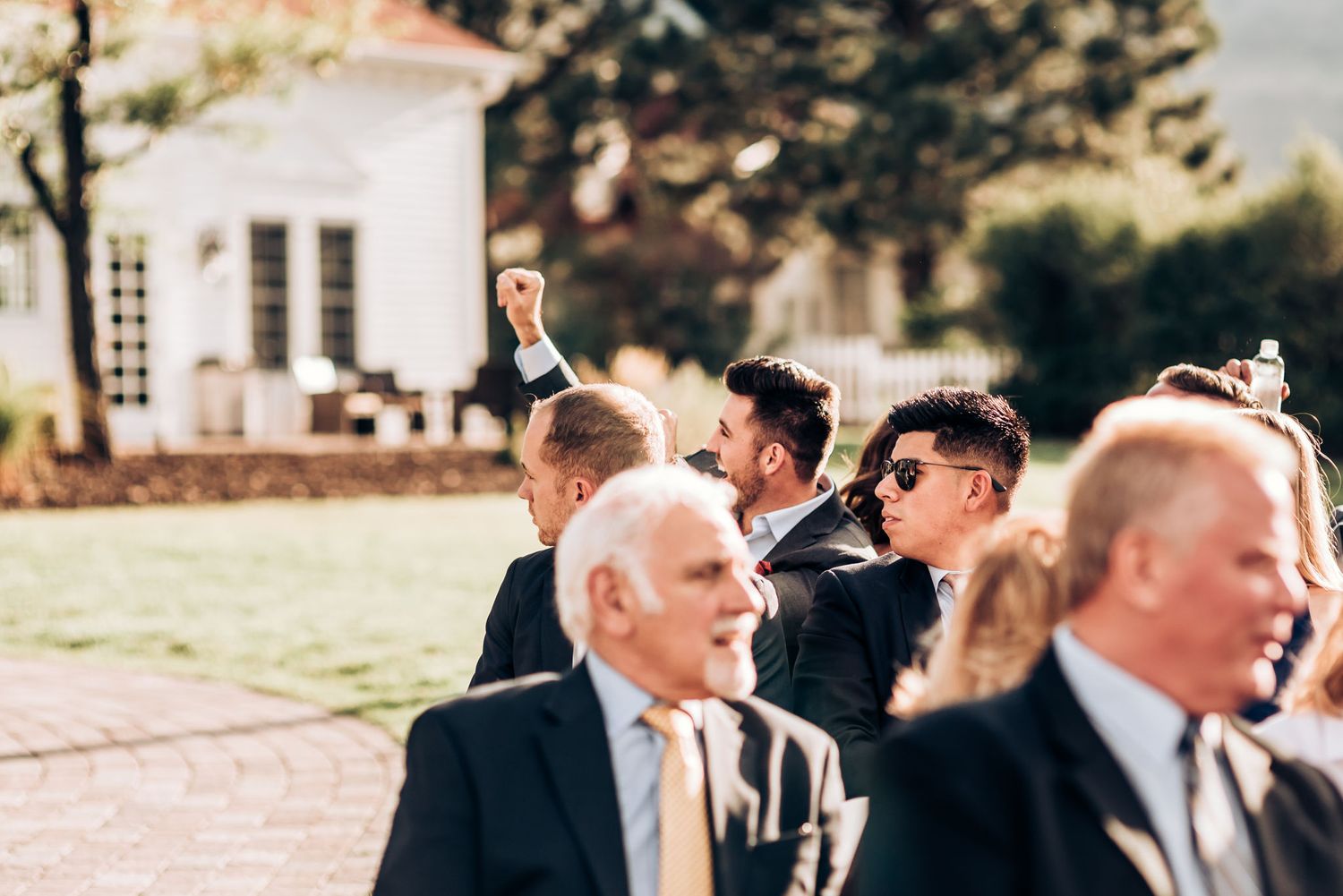 Wedding guests in formal attire gathered outdoors during a sunny afternoon celebration.