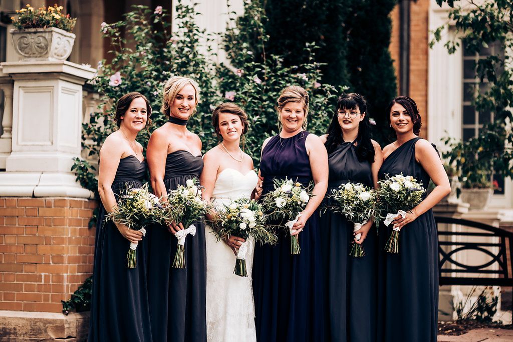 Wedding party in navy dresses poses together outdoors with matching bouquets.
