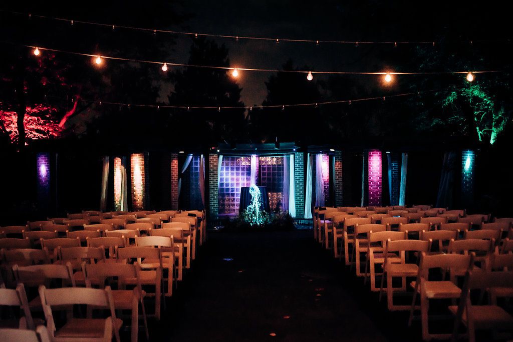 Indoor wedding ceremony venue with rows of white chairs and colorful stage lighting creating a dramatic ambiance.