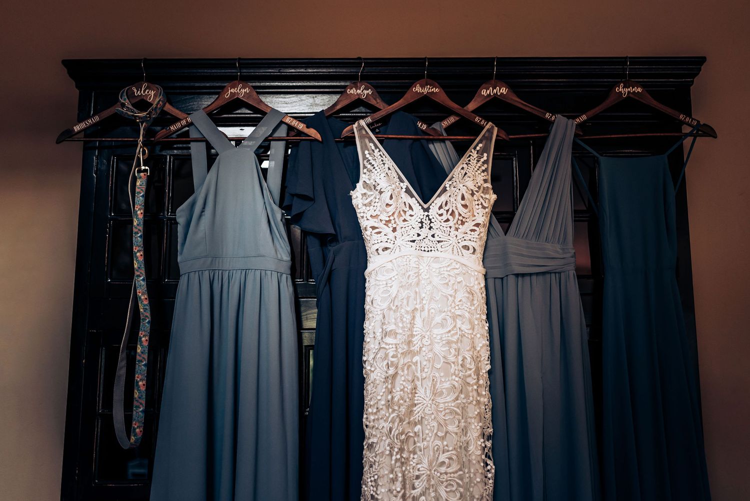 Wedding dress and bridesmaid dresses in blue tones hanging on wood wall.