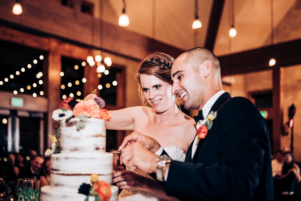 Newlyweds share a playful moment while cutting their tiered wedding cake.