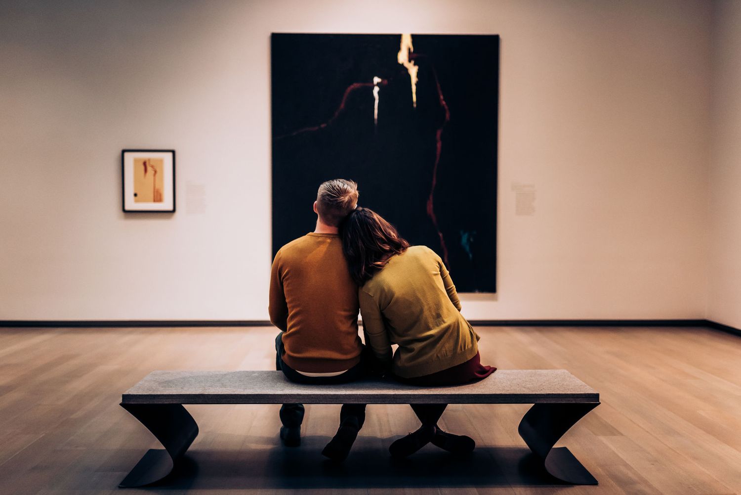 Two people sitting on bench viewing dramatic black artwork in museum.