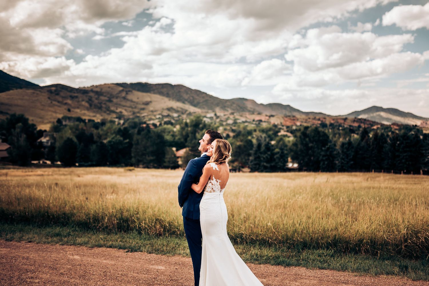 Romantic wedding embrace on mountain path with golden field backdrop.