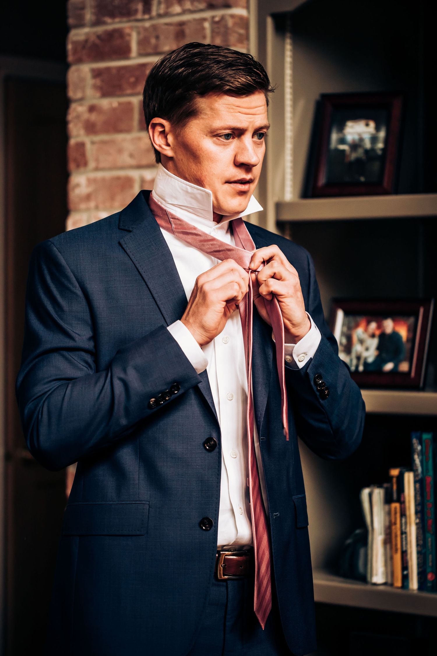 Man in navy suit adjusting his pink tie while getting ready.