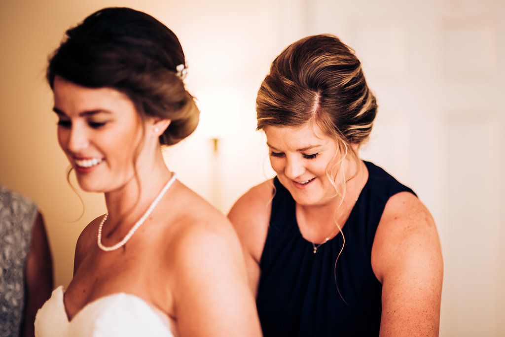 Two elegantly dressed women share a joyful moment while getting ready for a wedding celebration.
