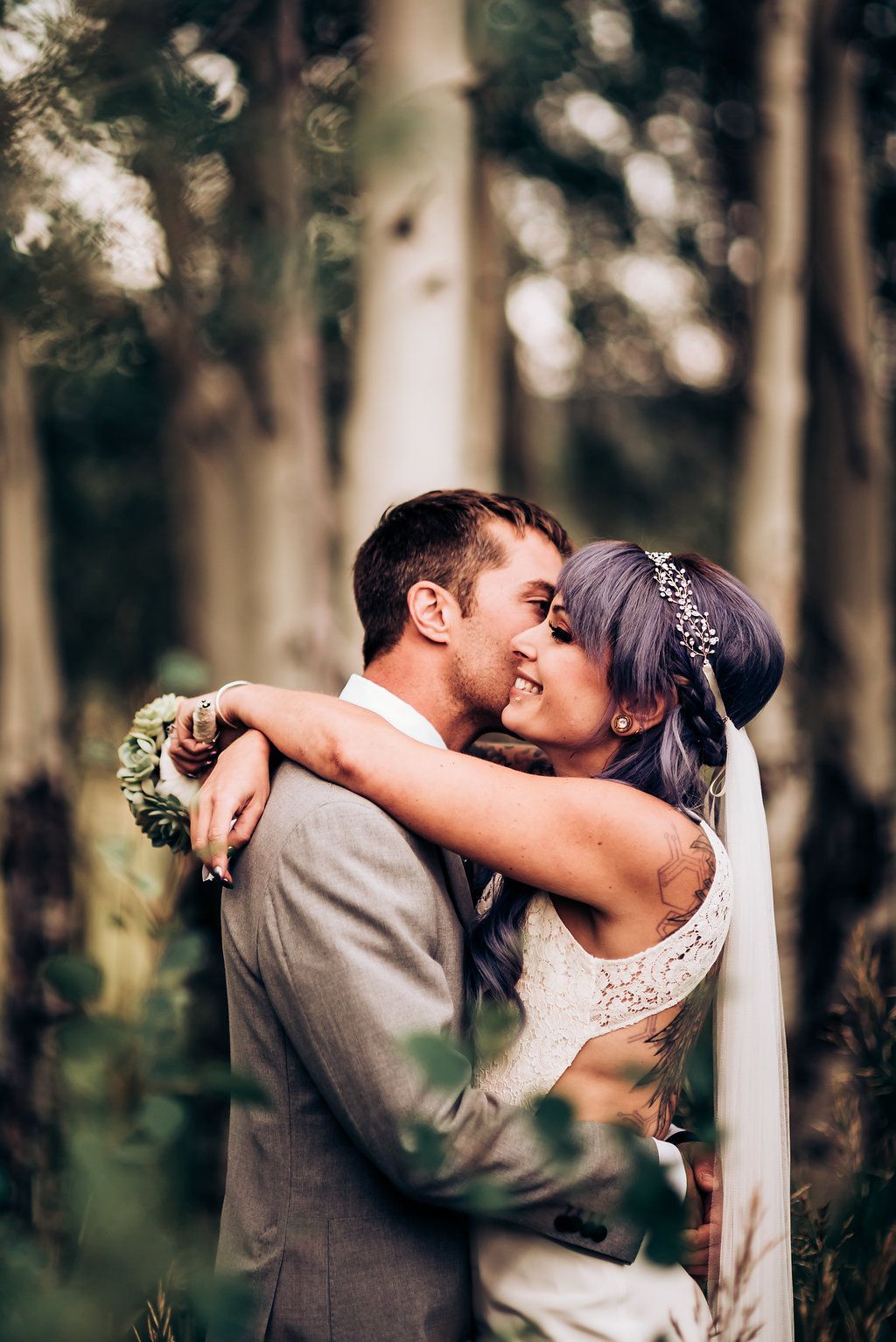 Romantic woodland wedding portrait with couple embracing among tall trees.