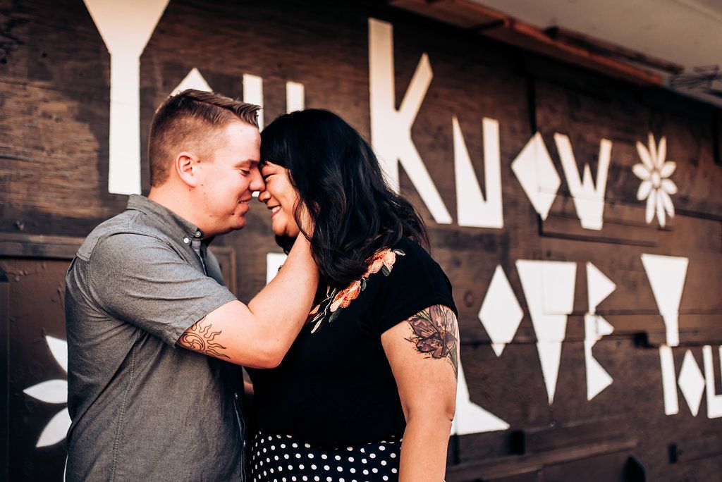 Couple shares intimate moment against rustic wooden wall with text artwork.